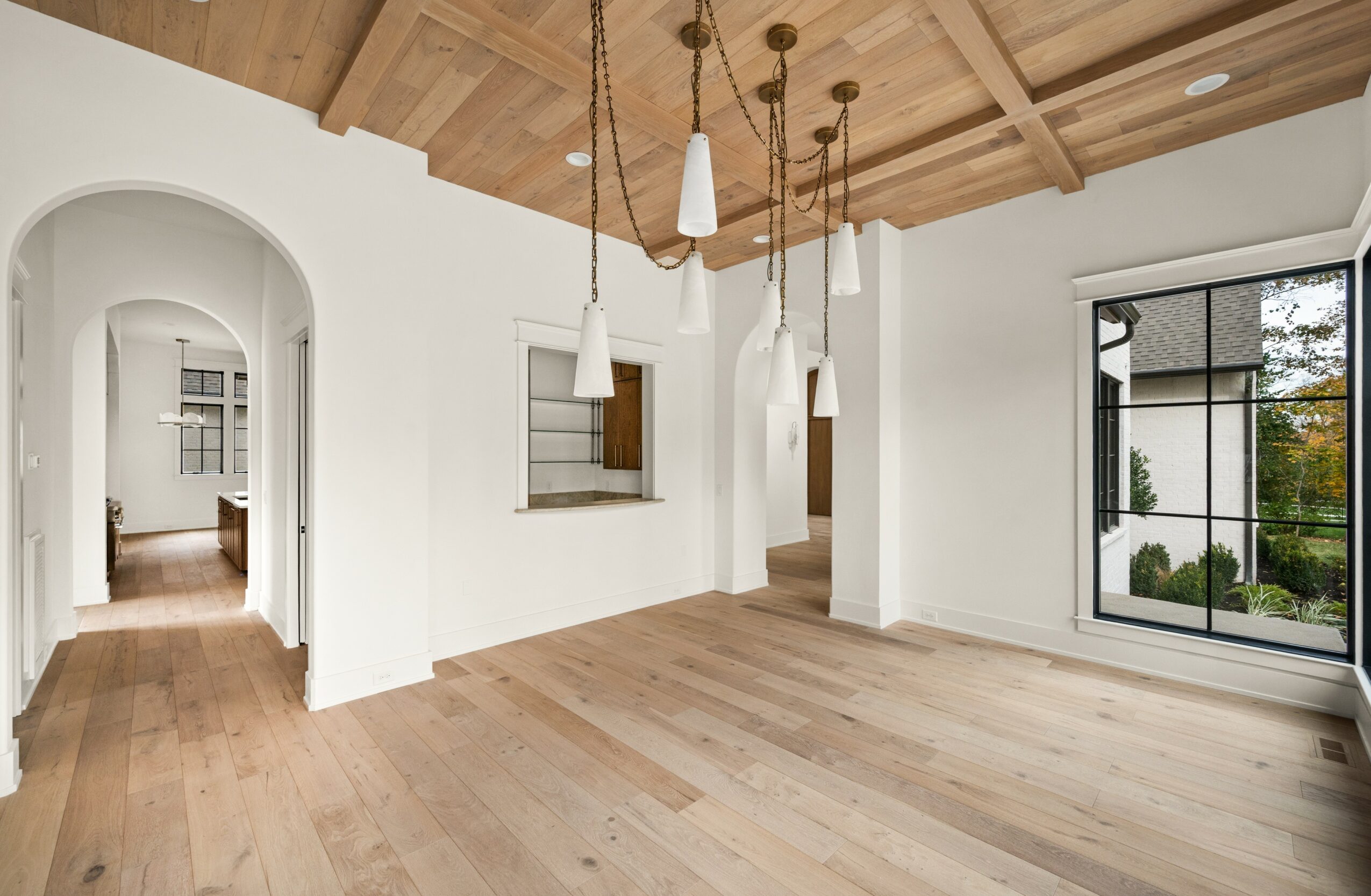Empty room with wooden ceiling, hanging lights, large window, and light wood flooring.