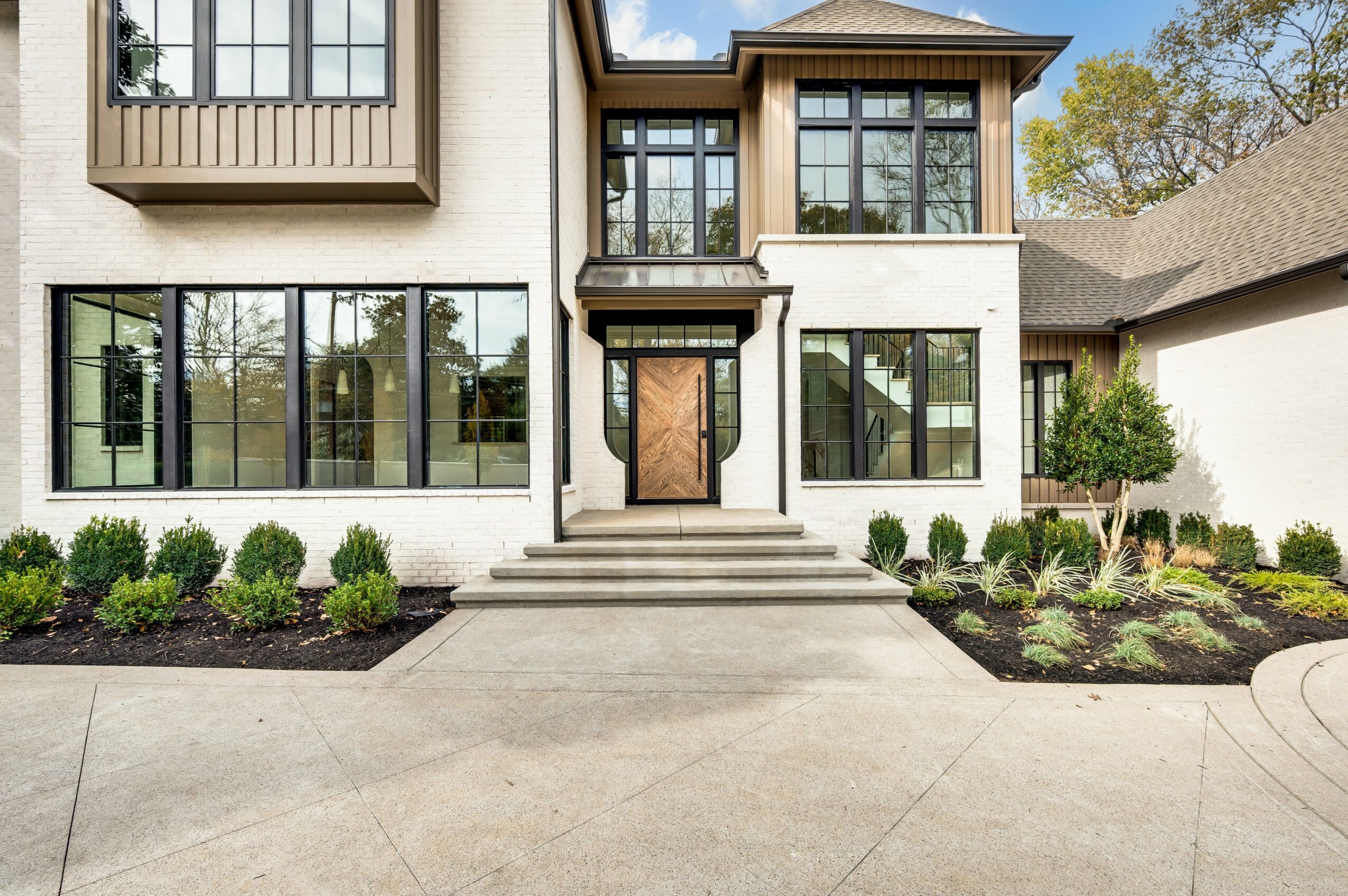Front view of a modern house with large windows, a wooden front door, and landscaped garden beds on each side.
