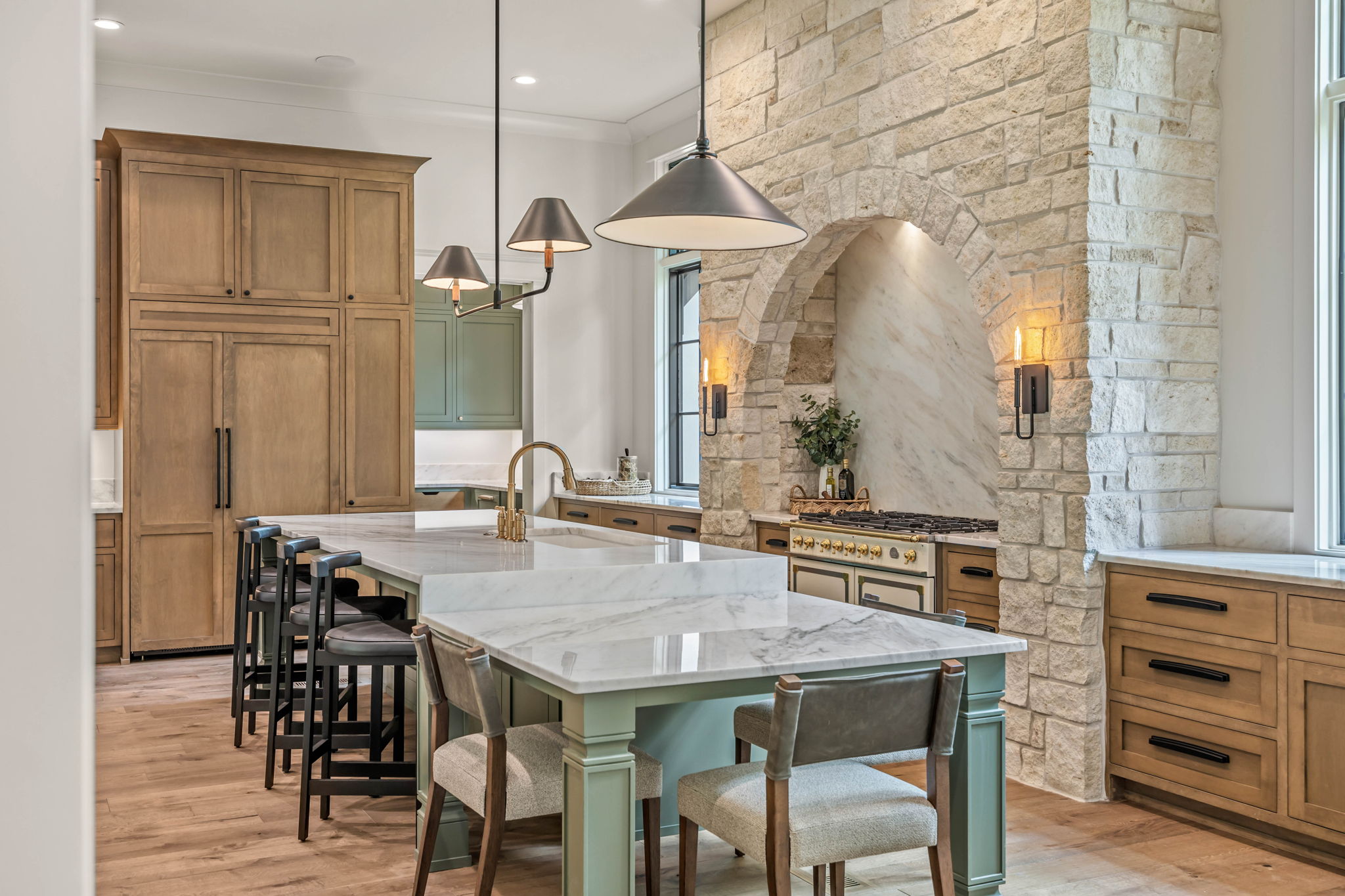 Kitchen with wooden cabinets, a marble island, pendant lights, stone wall, and window seating area.