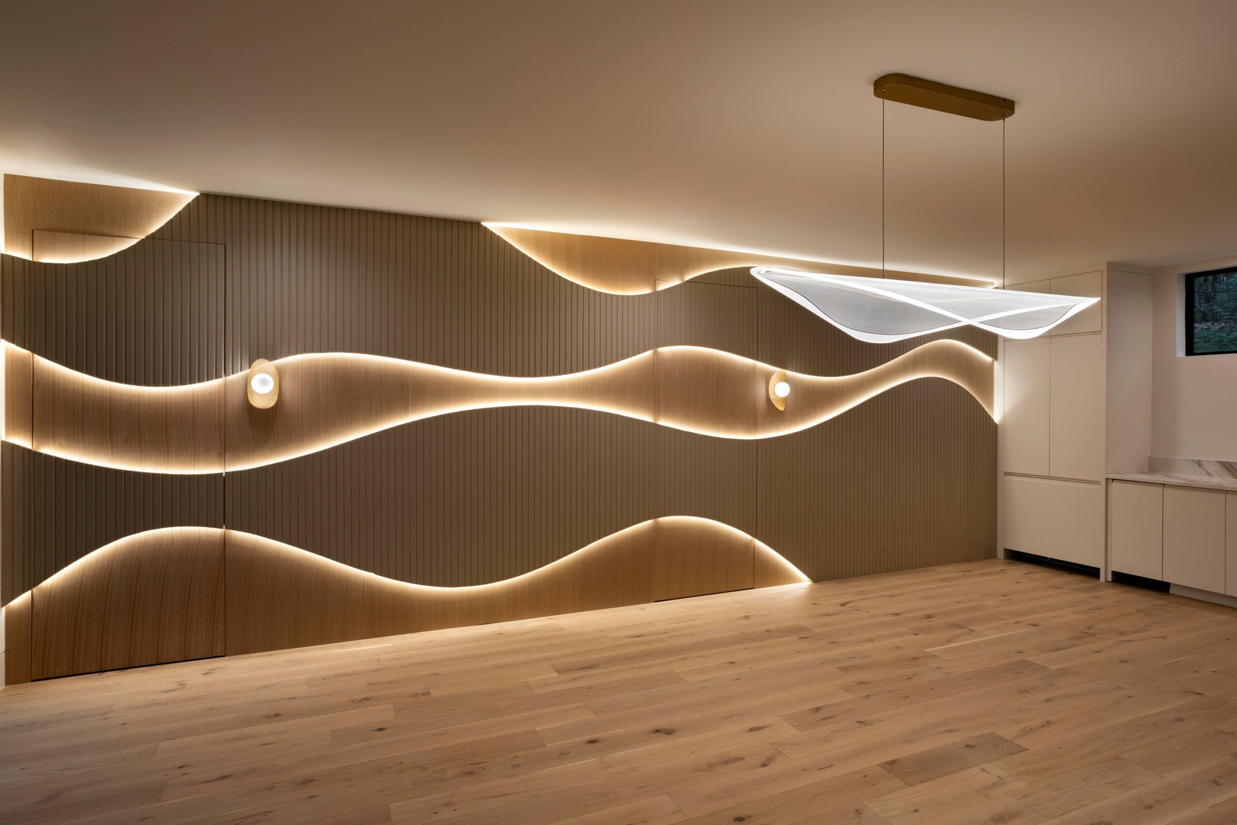 Modern interior wall with wavy illuminated design, ceiling light fixture, and wooden floor.