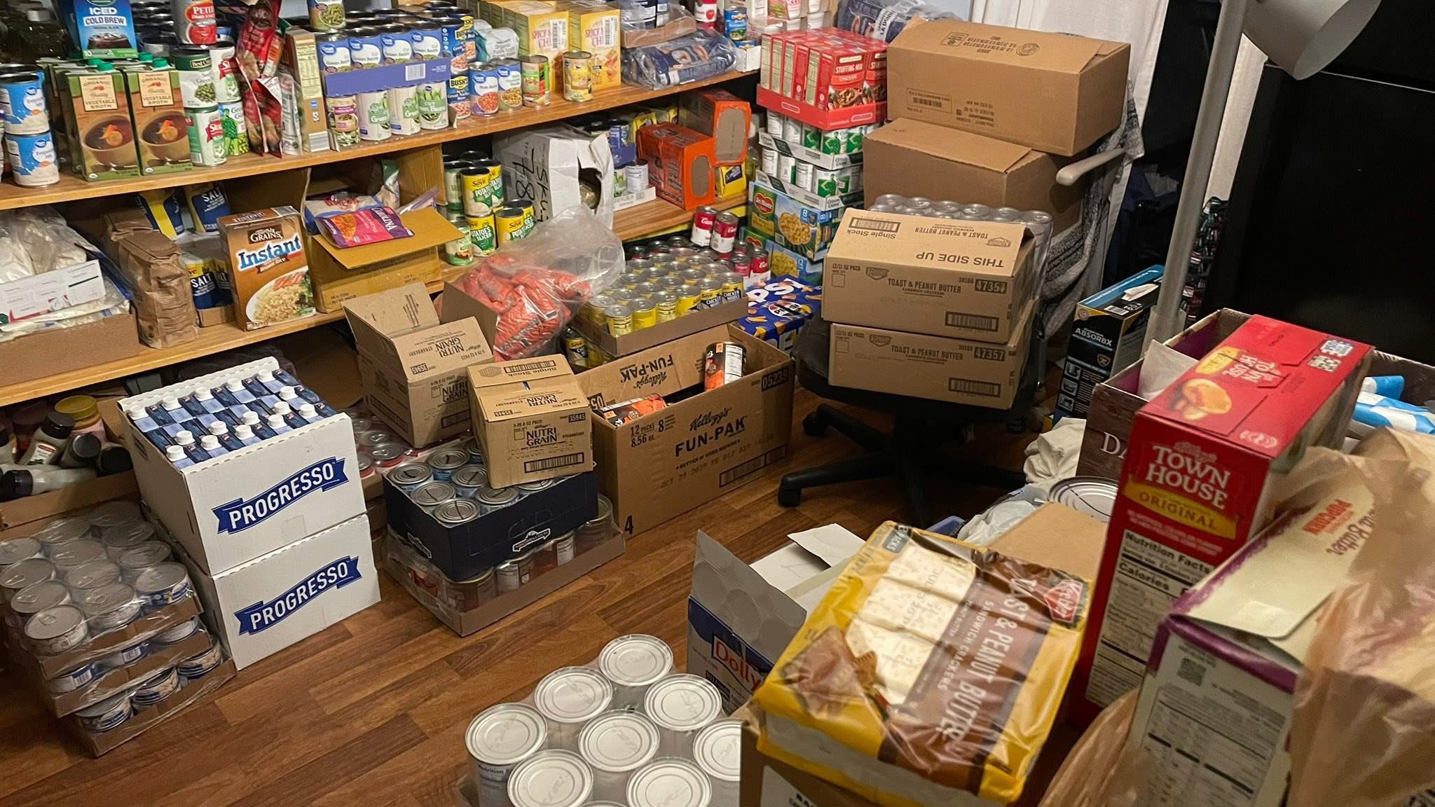 Room filled with shelves and boxes of food items, some stacked on the floor, cluttered and disorganized.