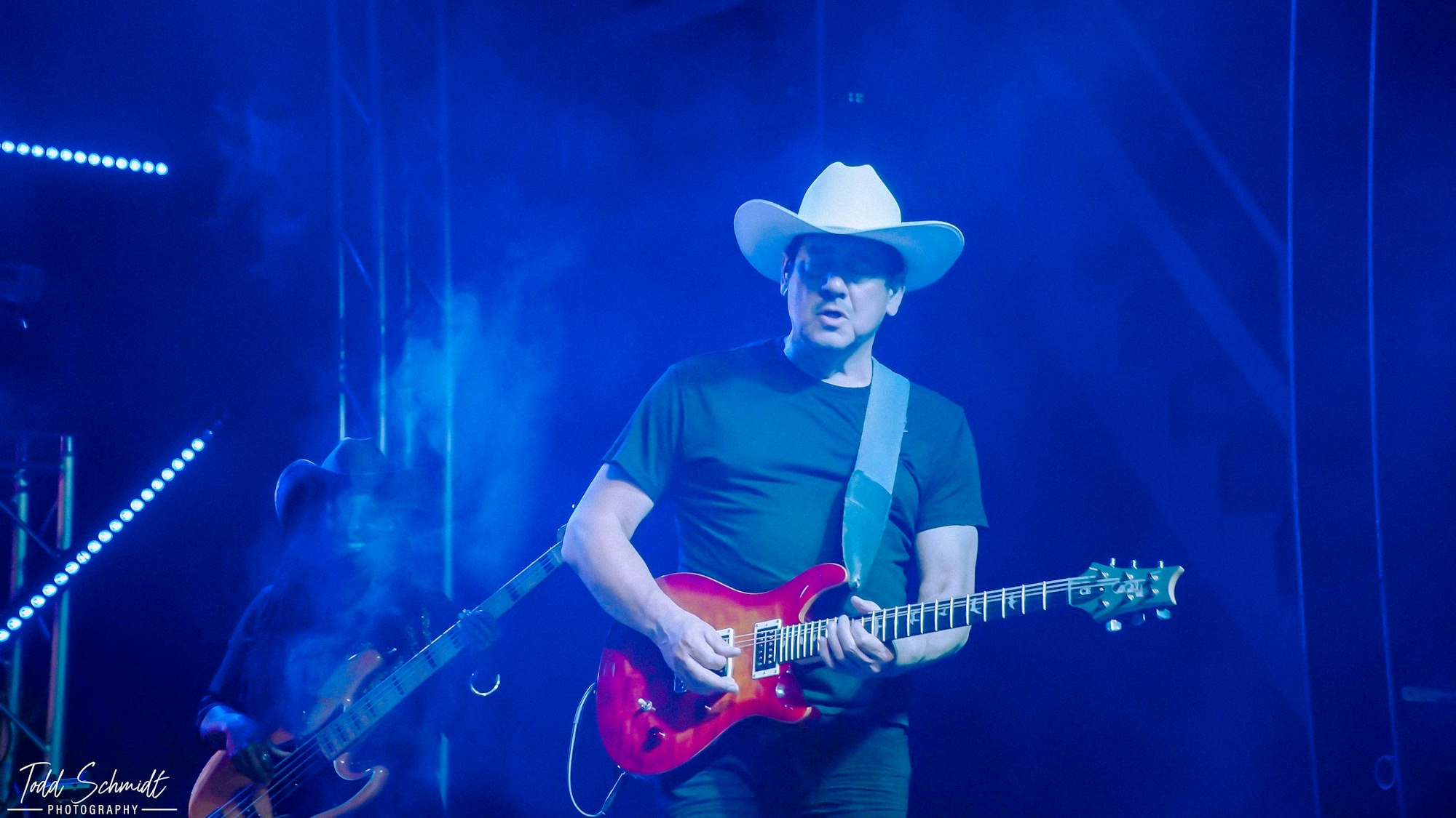 Person wearing a cowboy hat playing a red electric guitar on stage with blue lighting