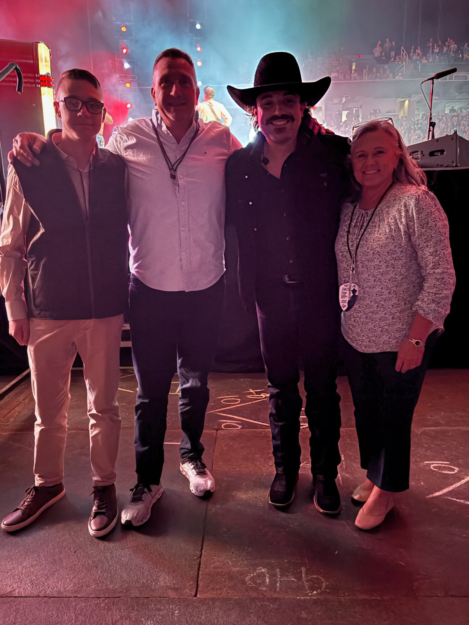 Four people standing together in a dimly lit setting with colorful lights, smiling at the camera.