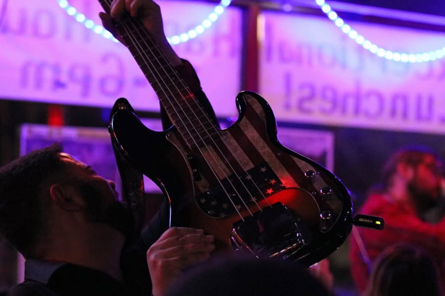 Person holding a guitar in a dimly lit, colorful setting with purple and pink lights, and blurred background.
