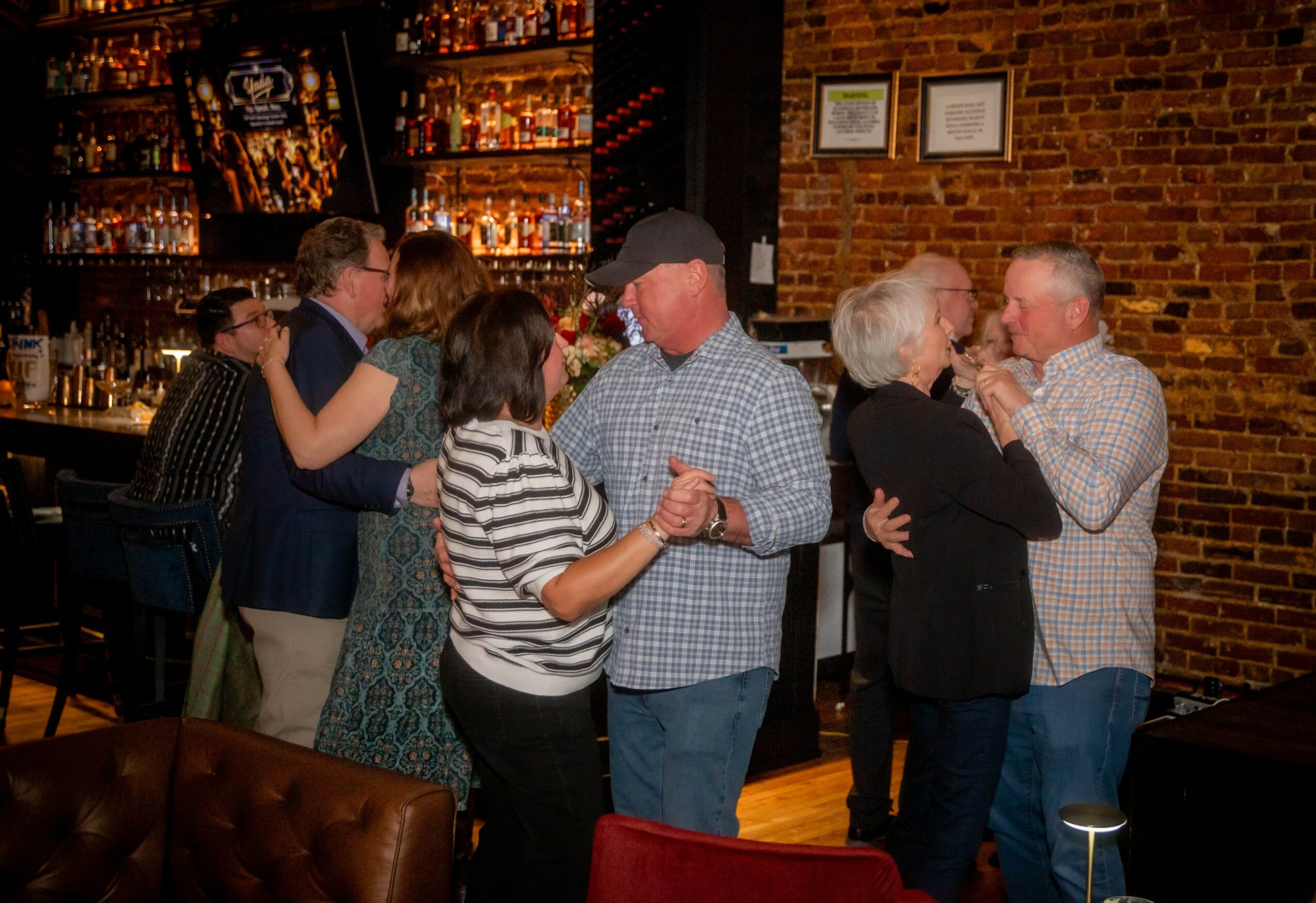 People dancing and socializing in a bar with brick walls and warm lighting.