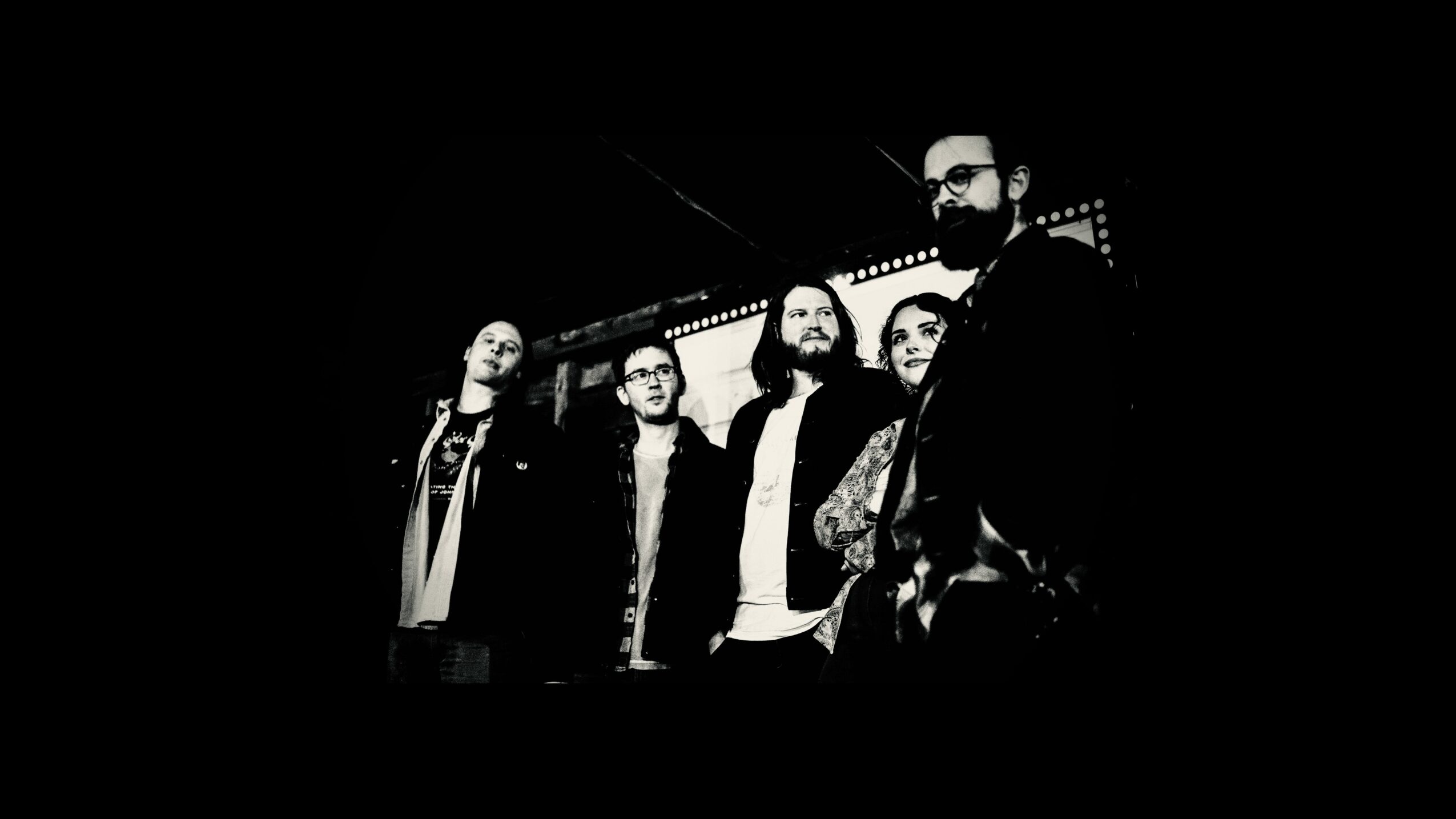 Five people standing together in front of a lit sign, black and white photo, some wearing glasses, casual clothing.