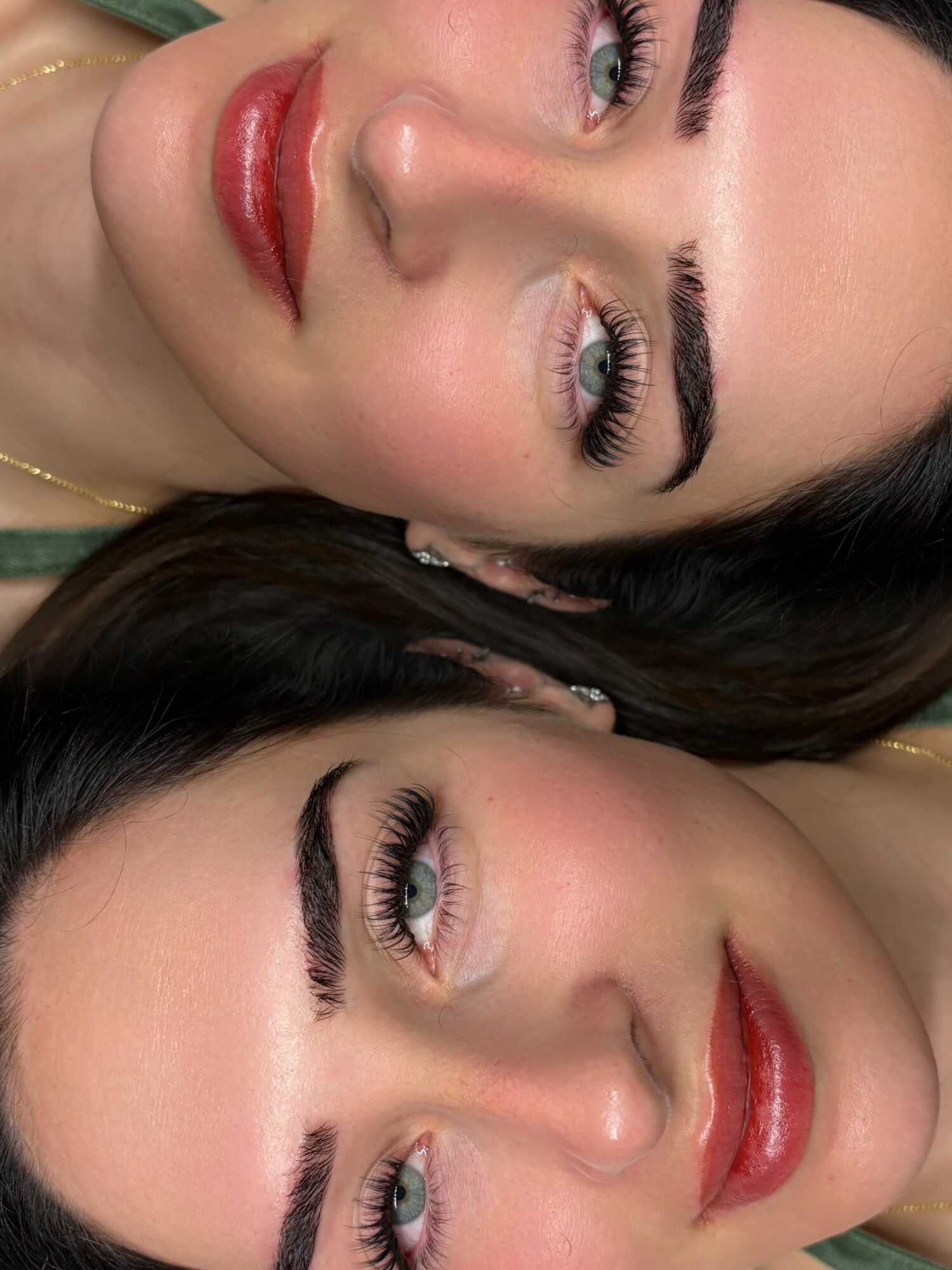 Two women with makeup and dark hair lying close, faces turned upward, smiling, with visible makeup and jewelry.