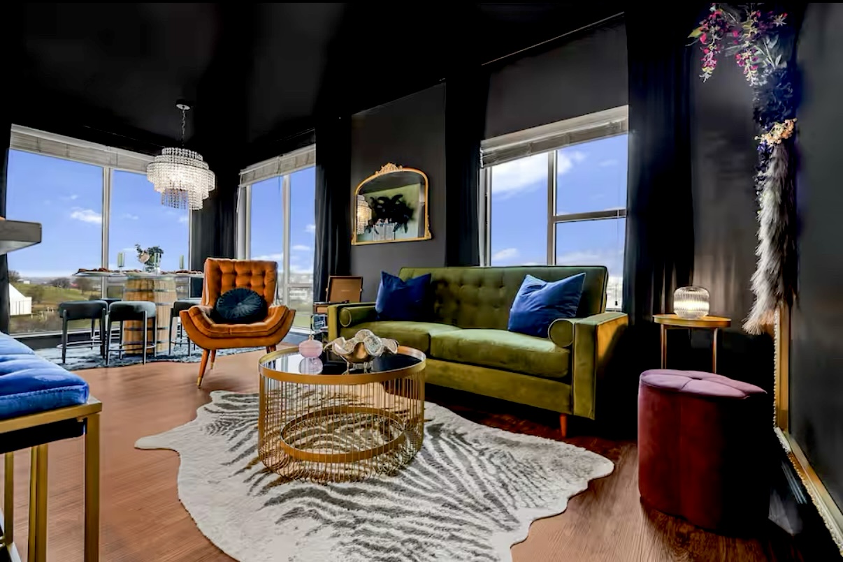 Living room with large windows, colorful furniture, a zebra-patterned rug, and decorative items, bright daylight outside.