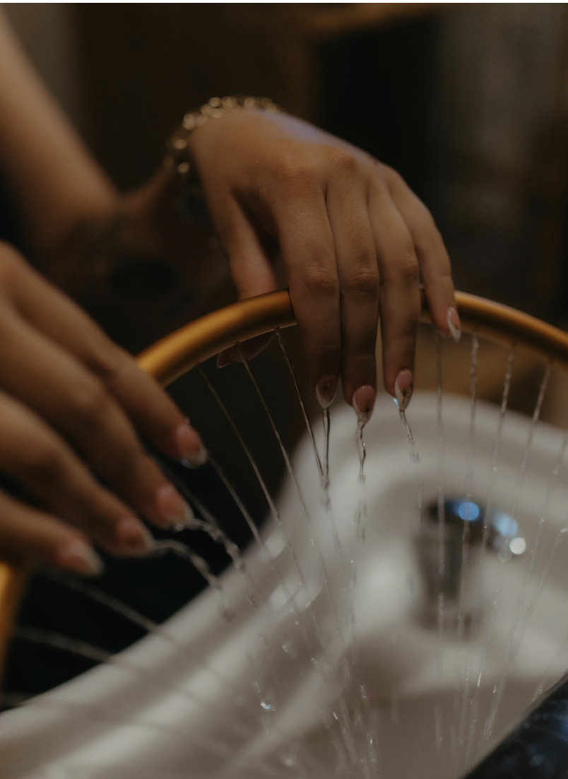 Hands washing a yellow bicycle handlebar over a sink with water running, in a dimly lit setting.