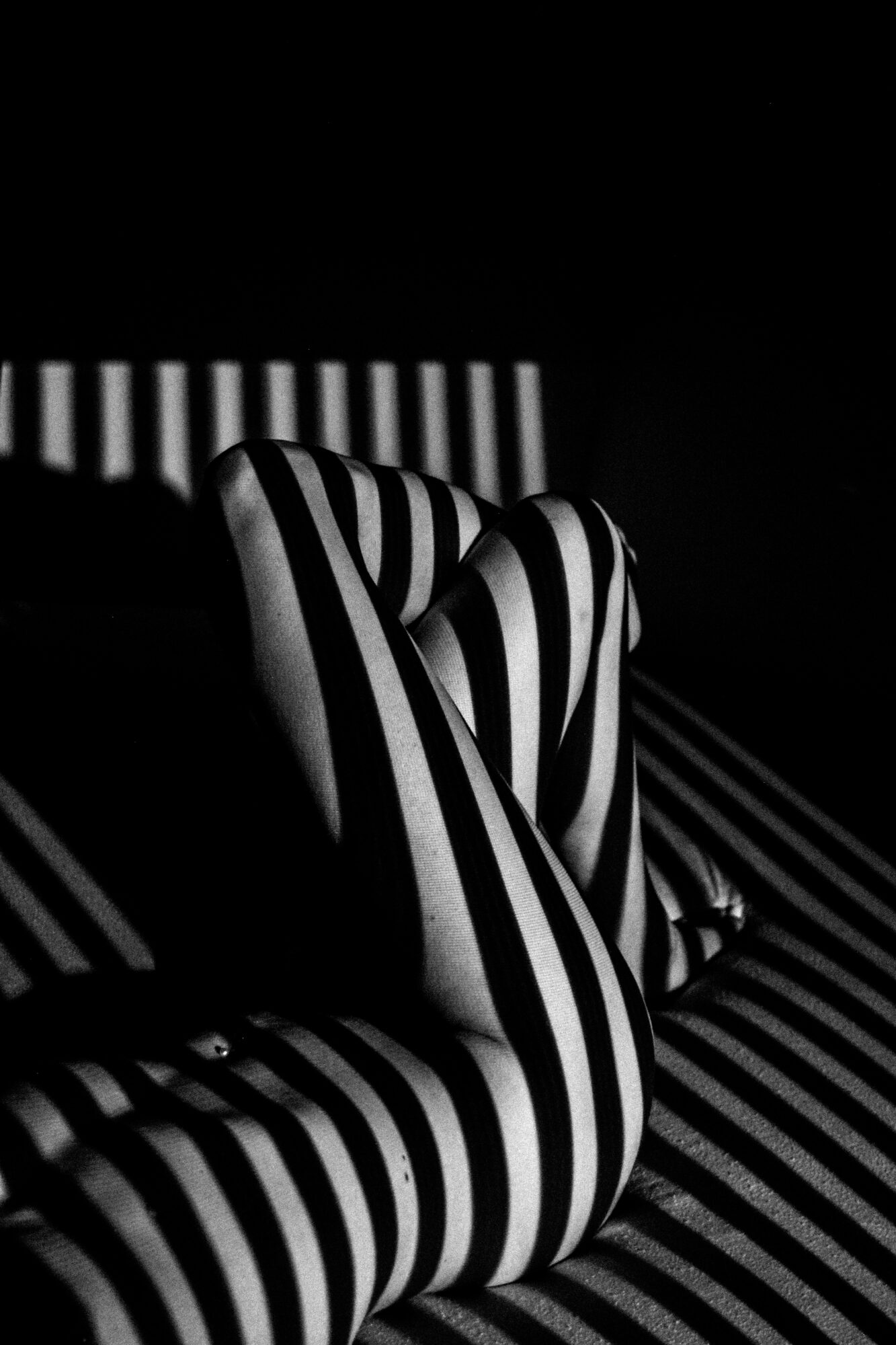 Person lying on striped surface with striped clothing, head turned away, in black and white lighting, creating high contrast patterns.