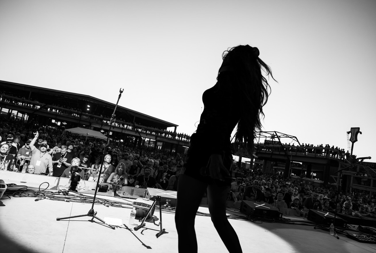 Silhouette of a person with long hair on stage, audience in background, black and white image.