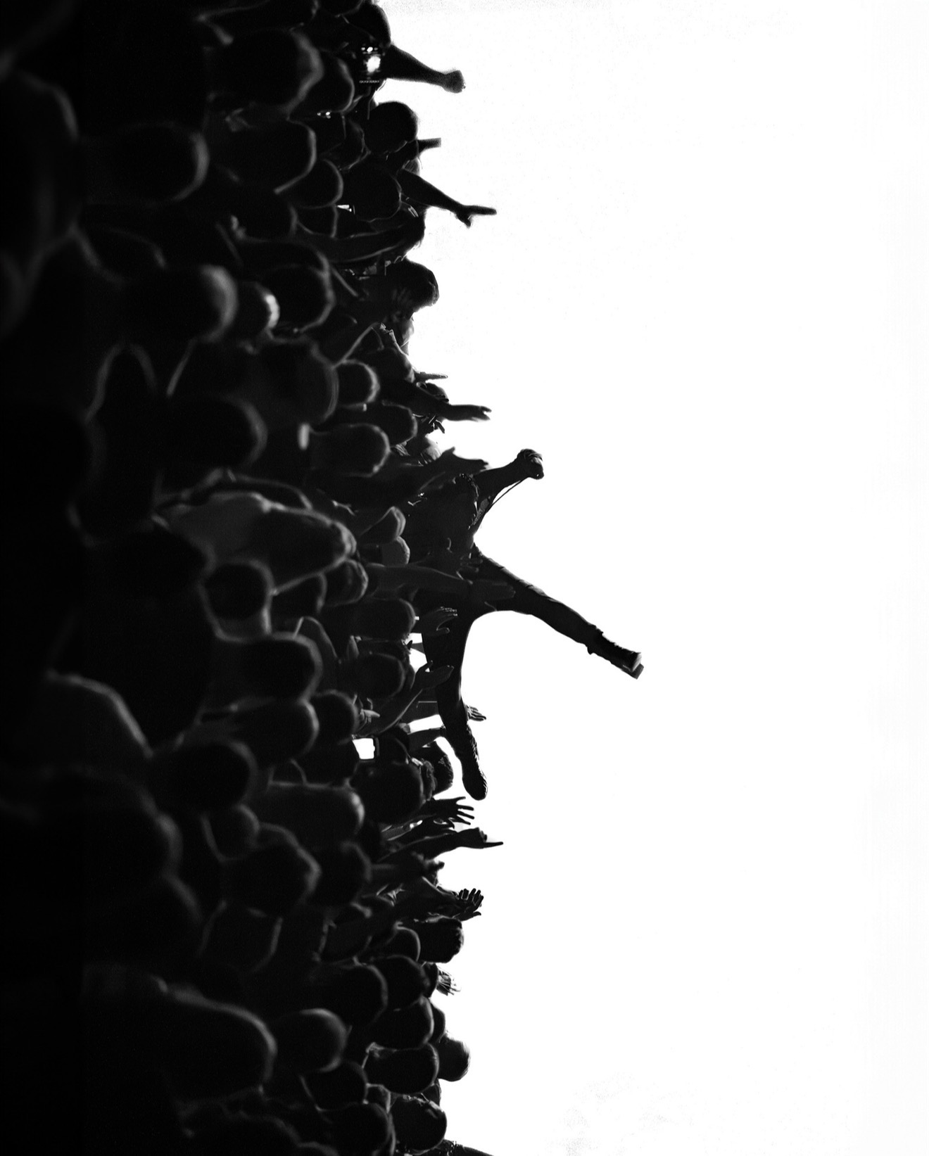 Silhouettes of people with arms raised against a bright sky, forming a crowd scene.