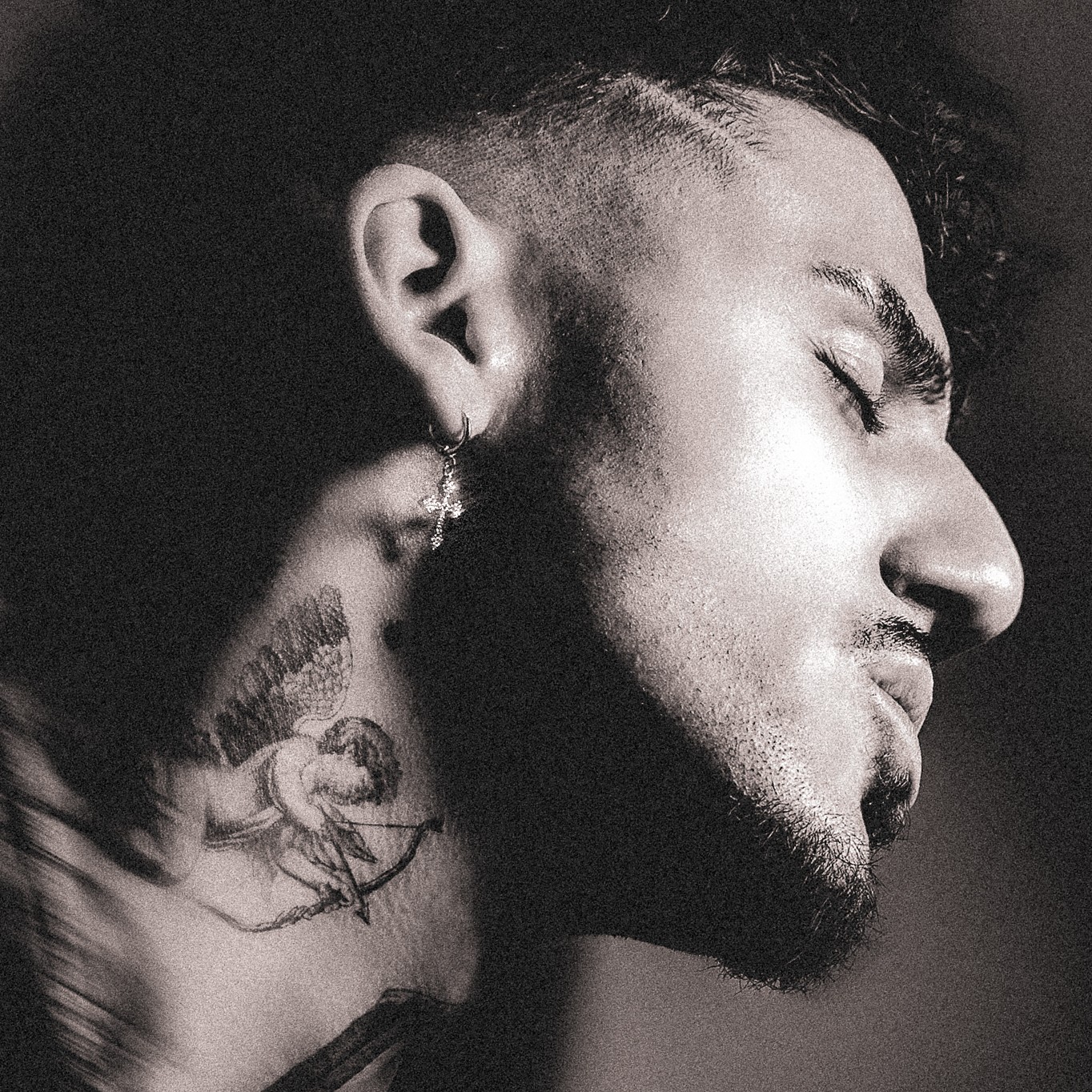 Close-up of a person's face in profile with eyes closed, showing facial hair, ear, and neck tattoo, in black and white.