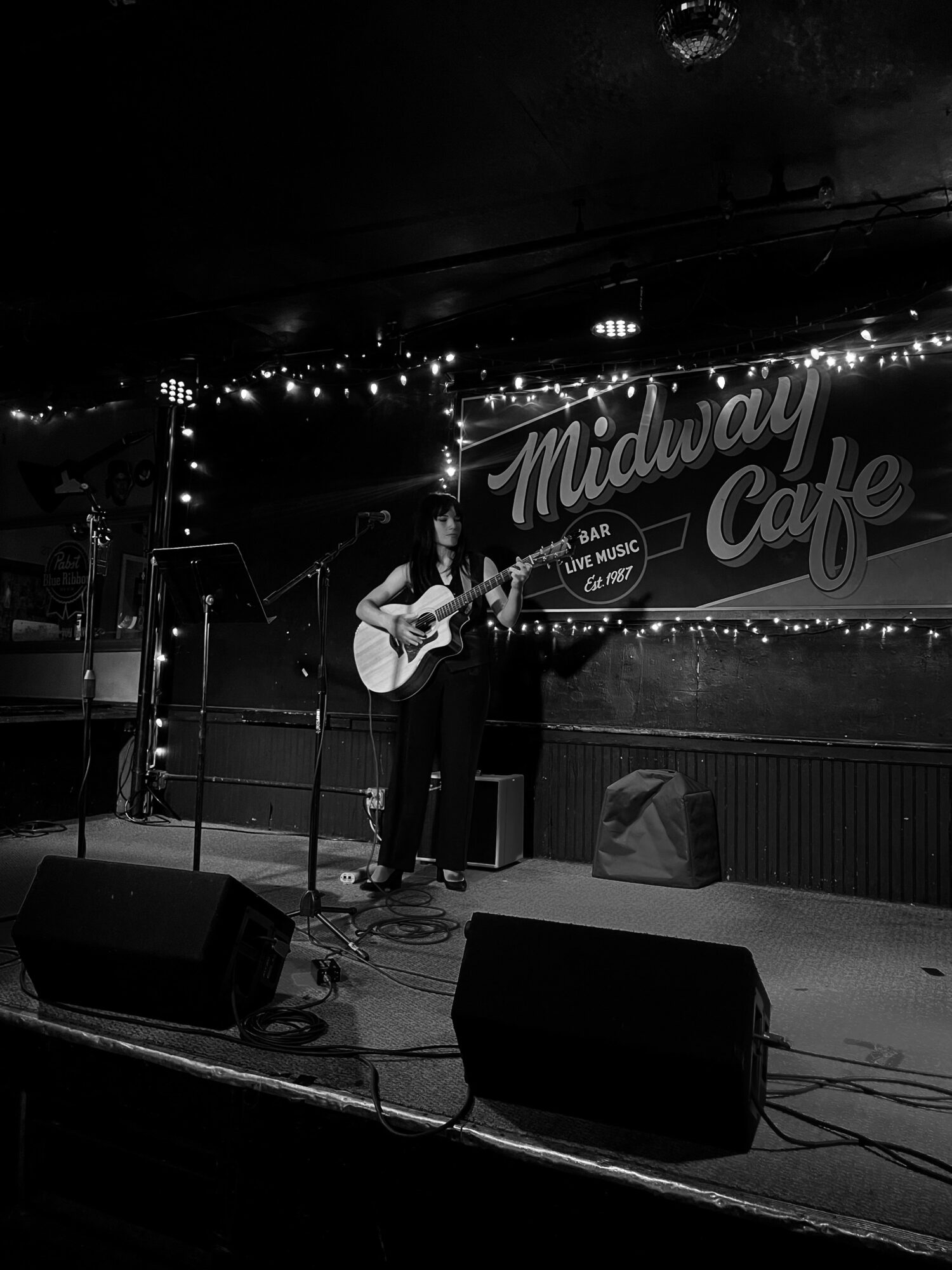 Two musicians perform on stage with guitars at Midnight Cafe, with a sign and string lights in the background.