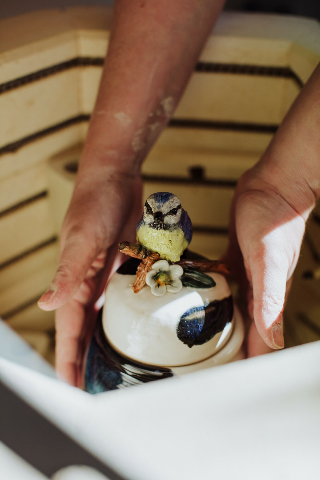 Person's hands holding a cake with a small bird figurine on top, against a wooden background.