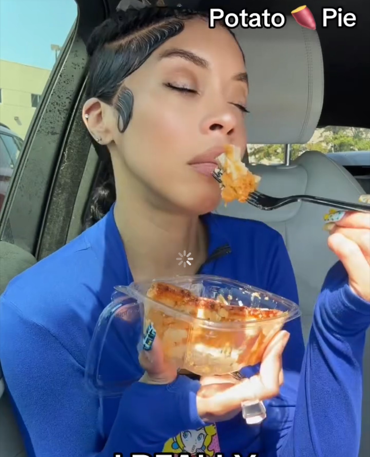 Woman with closed eyes eating potato pie from a bowl inside a car, wearing a blue top.