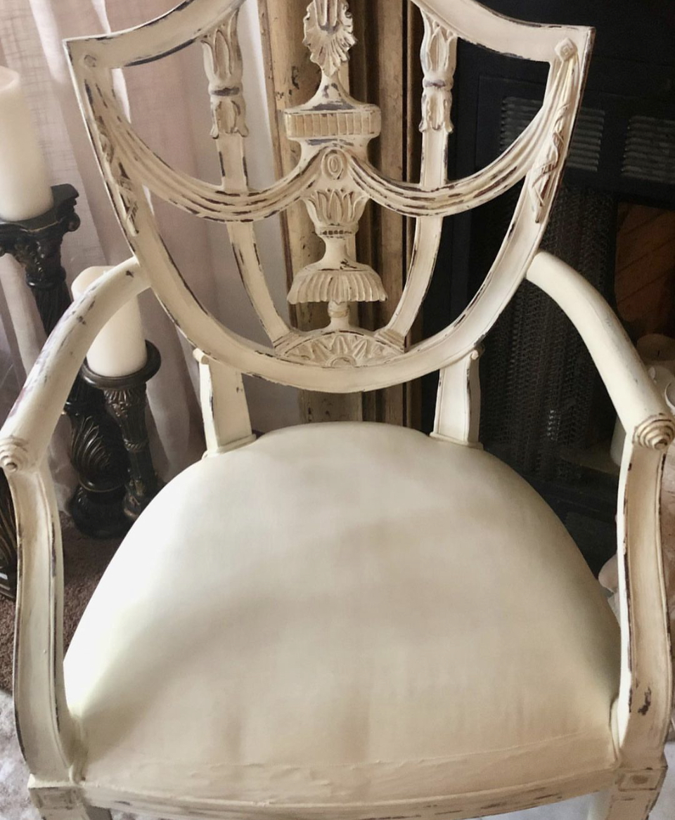 Upright antique-style chair with carved wooden backrest and cream-colored upholstery seat.