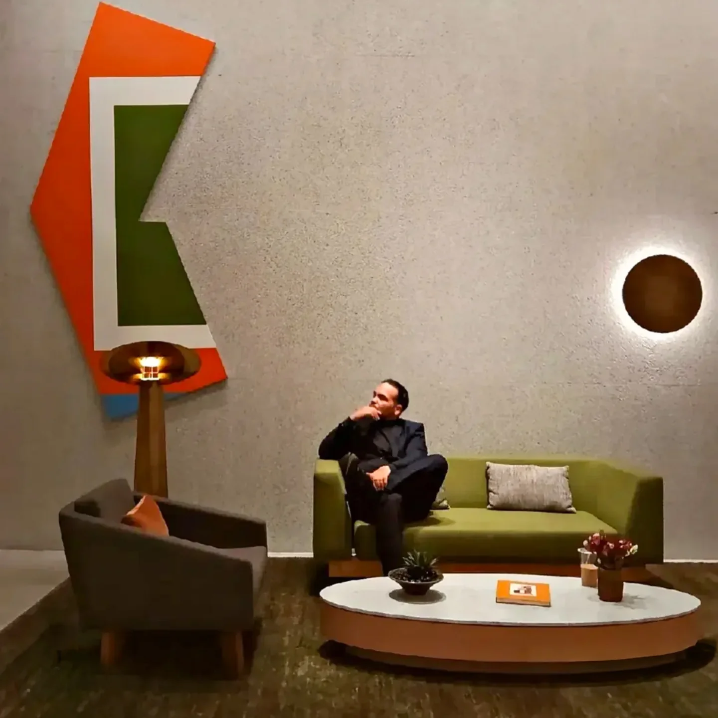 Person sitting on a green sofa in a modern room with a white wall, a round window, and colorful wall art.