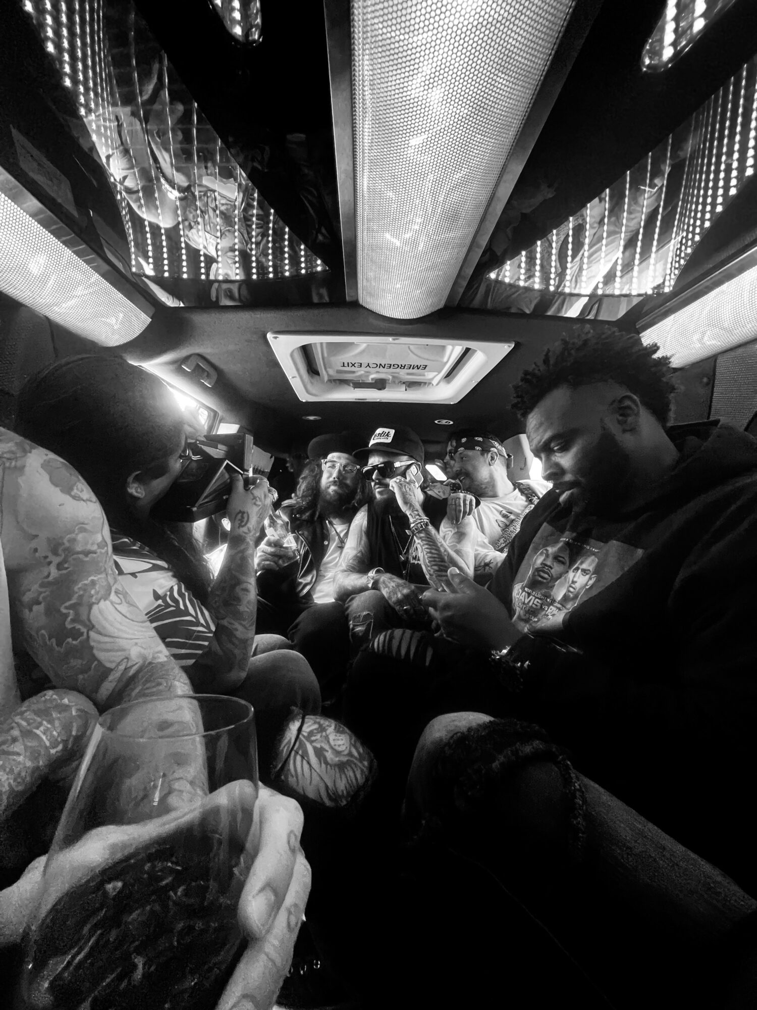 People sitting inside a vehicle, some using phones, with a ceiling featuring reflective panels and a central light fixture.