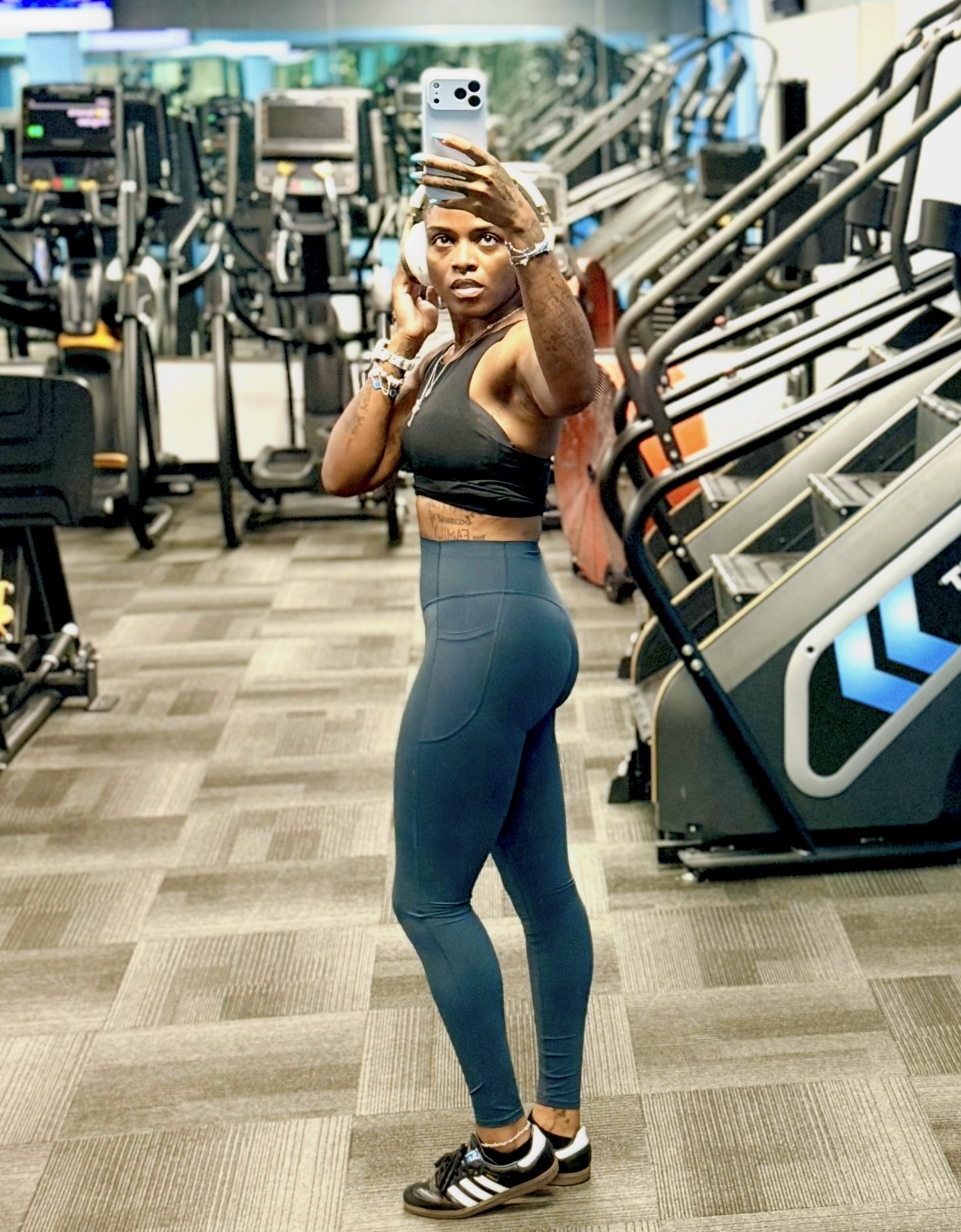 Woman taking a mirror selfie in a gym, wearing workout clothes, with exercise equipment in the background.