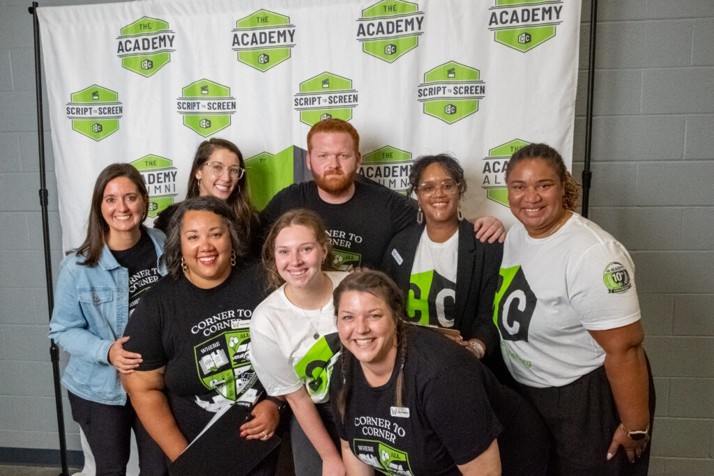 Group of seven people smiling, standing in front of a backdrop with 'Script- Screen' and 'Academy' logos, indoors.
