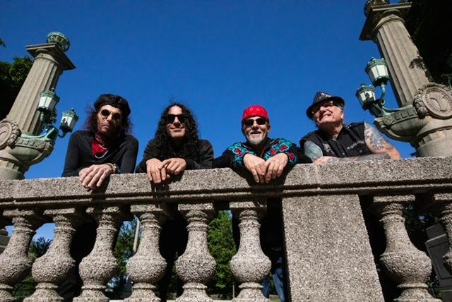 Four people leaning on a stone railing outdoors with a blue sky background.