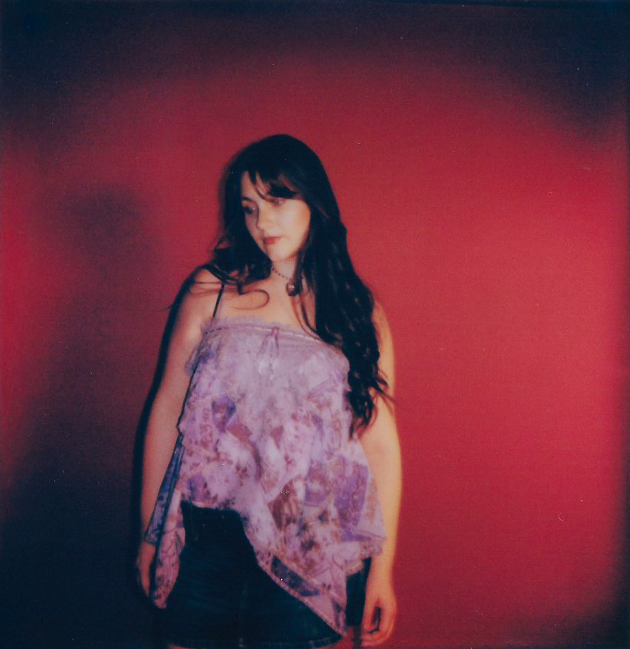 Woman with long dark hair wearing a purple top against a red background.