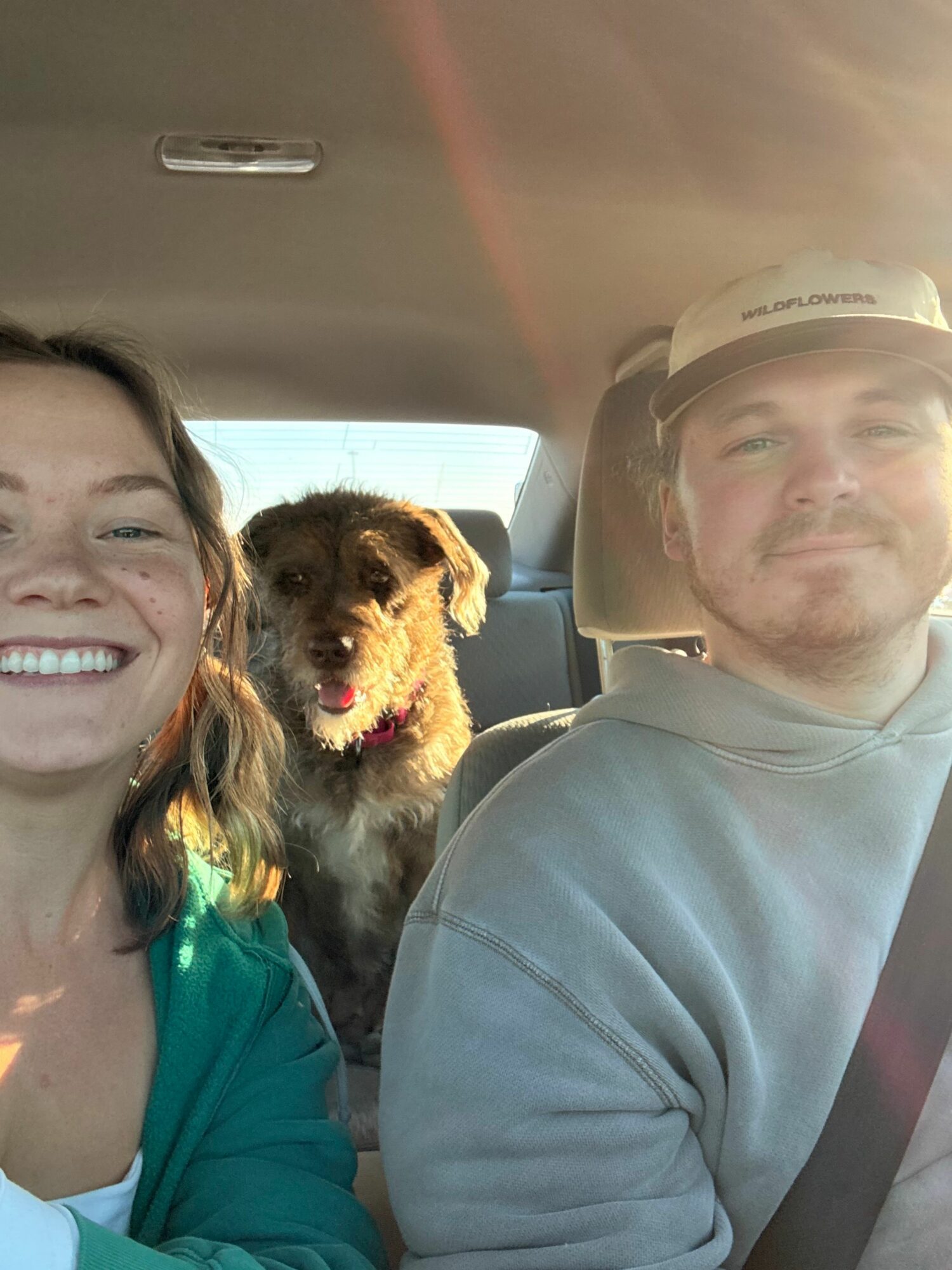 A man and a woman with a small dog inside a vehicle, smiling and looking at the camera.