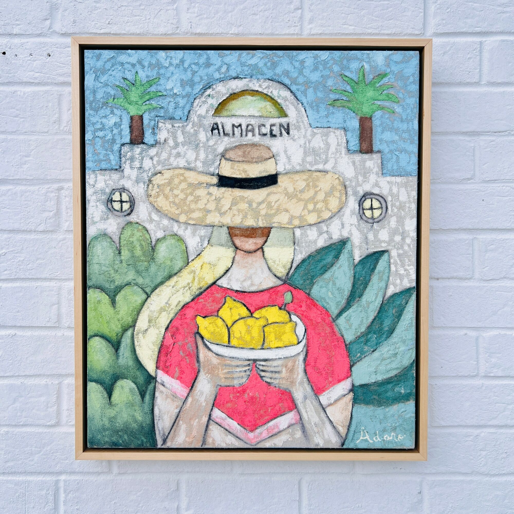 Person with a large hat holding a bowl of lemons, standing in front of a building with palm trees.