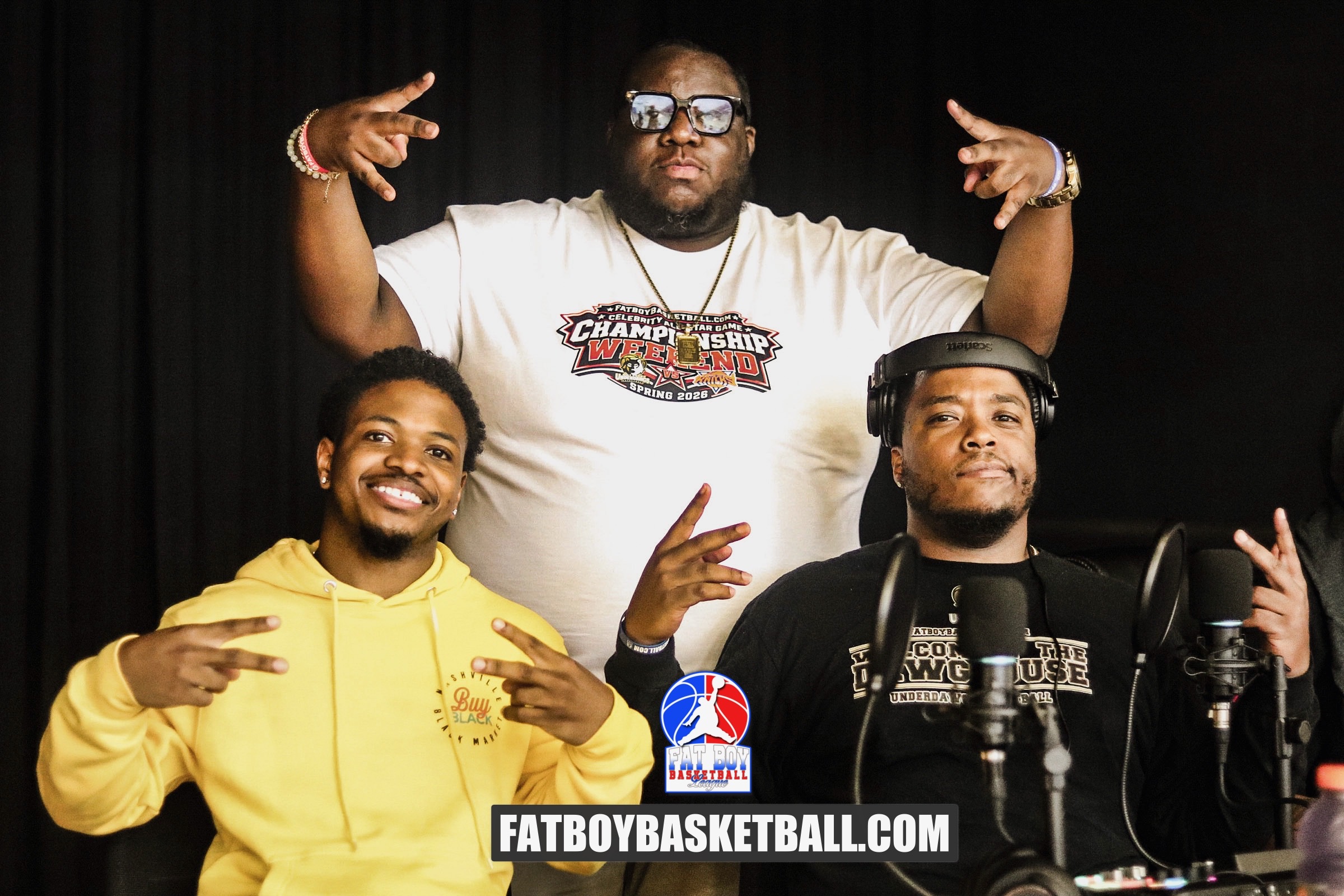 Three men pose in front of a black background, one in a white shirt, two in yellow and black, with microphones.