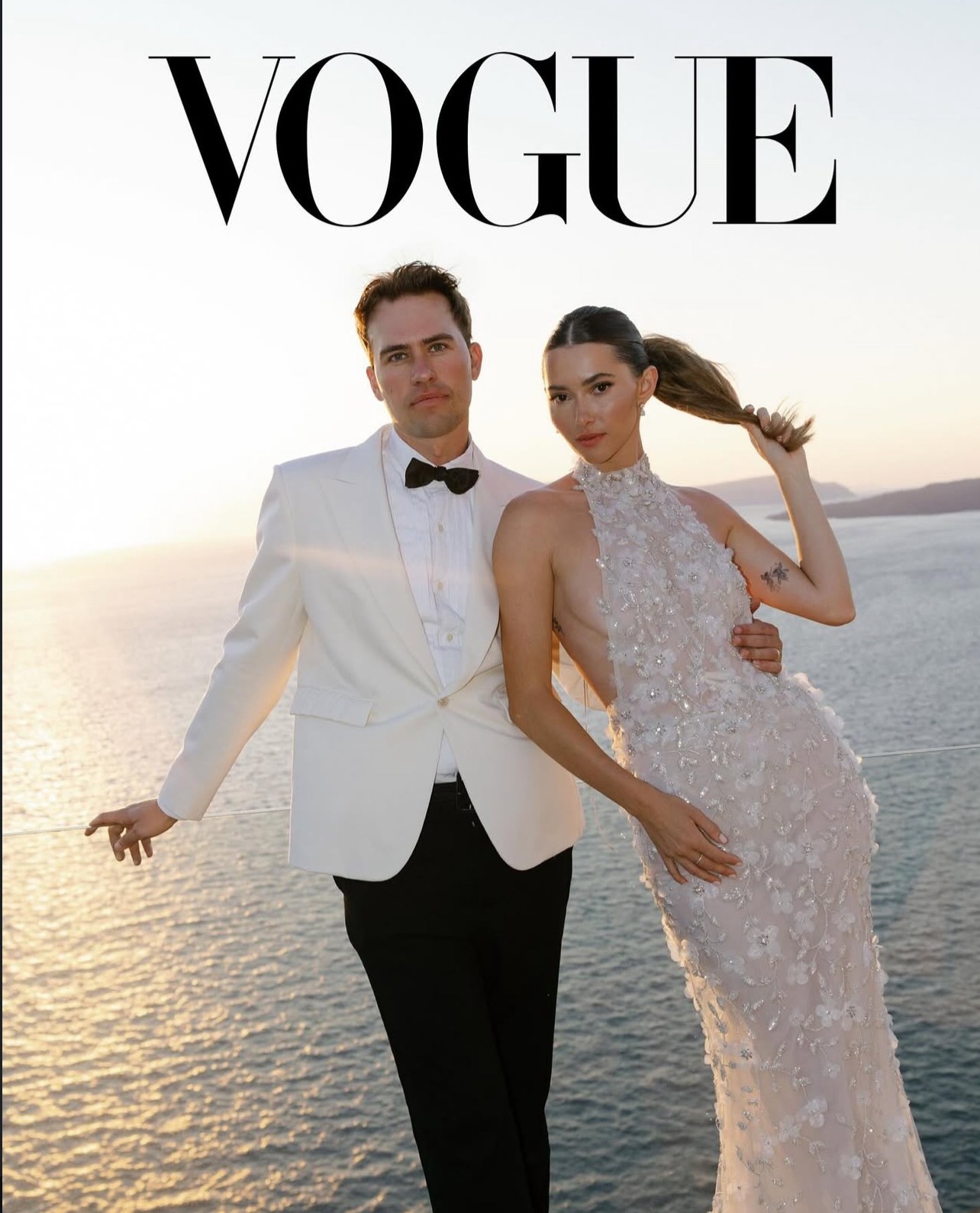 Man and woman in formal attire standing by water at sunset, Vogue magazine cover, woman in white gown, man in tuxedo.