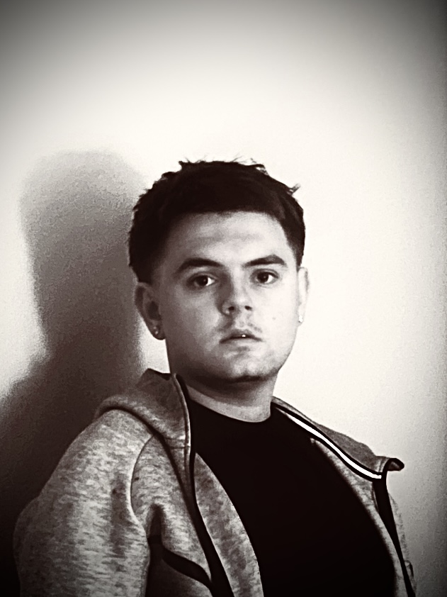 Young man with short dark hair wearing a hoodie and black shirt, looking at the camera, plain background.