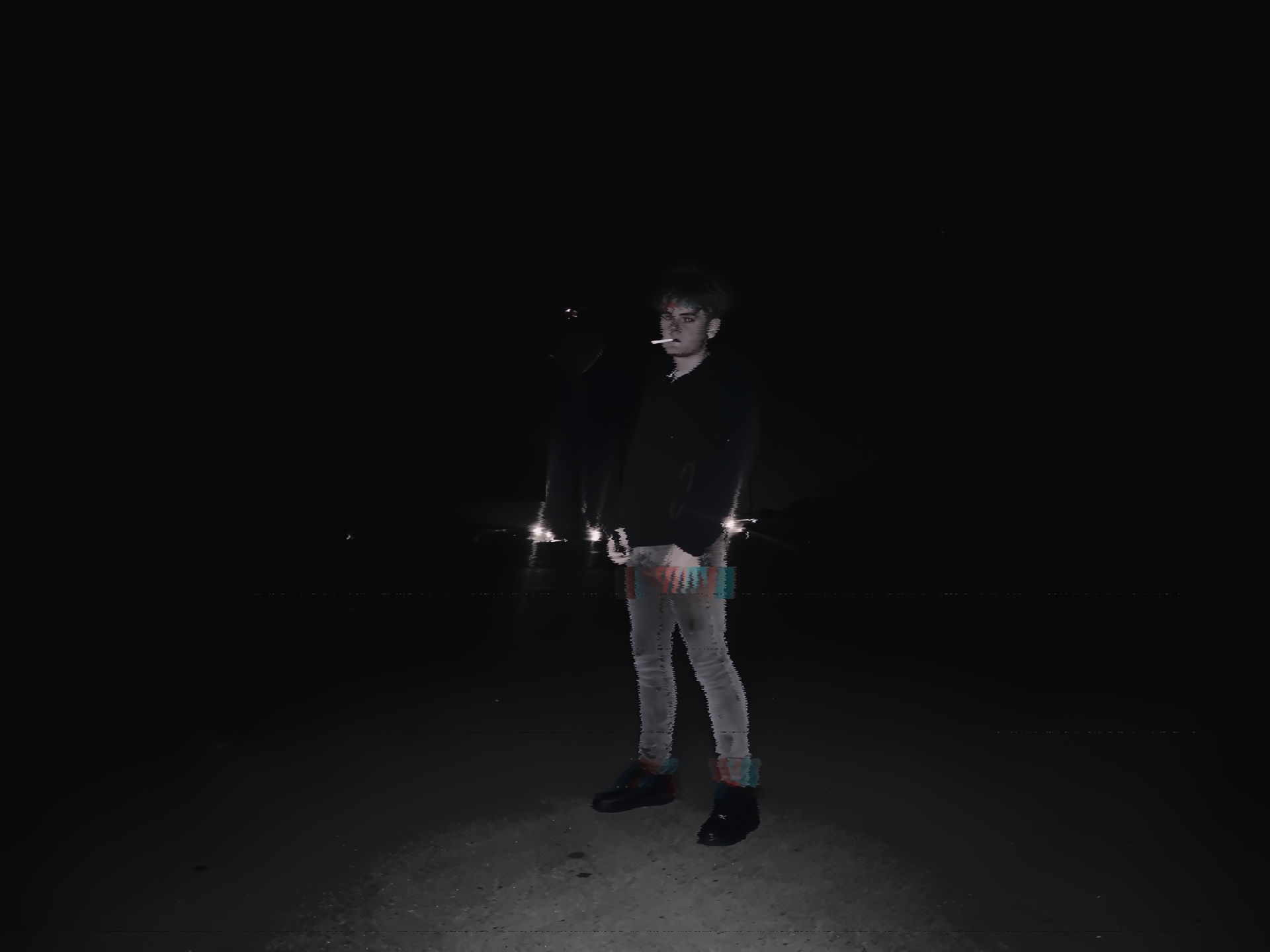 Person standing outdoors at night, illuminated by a light source, with a dark background.