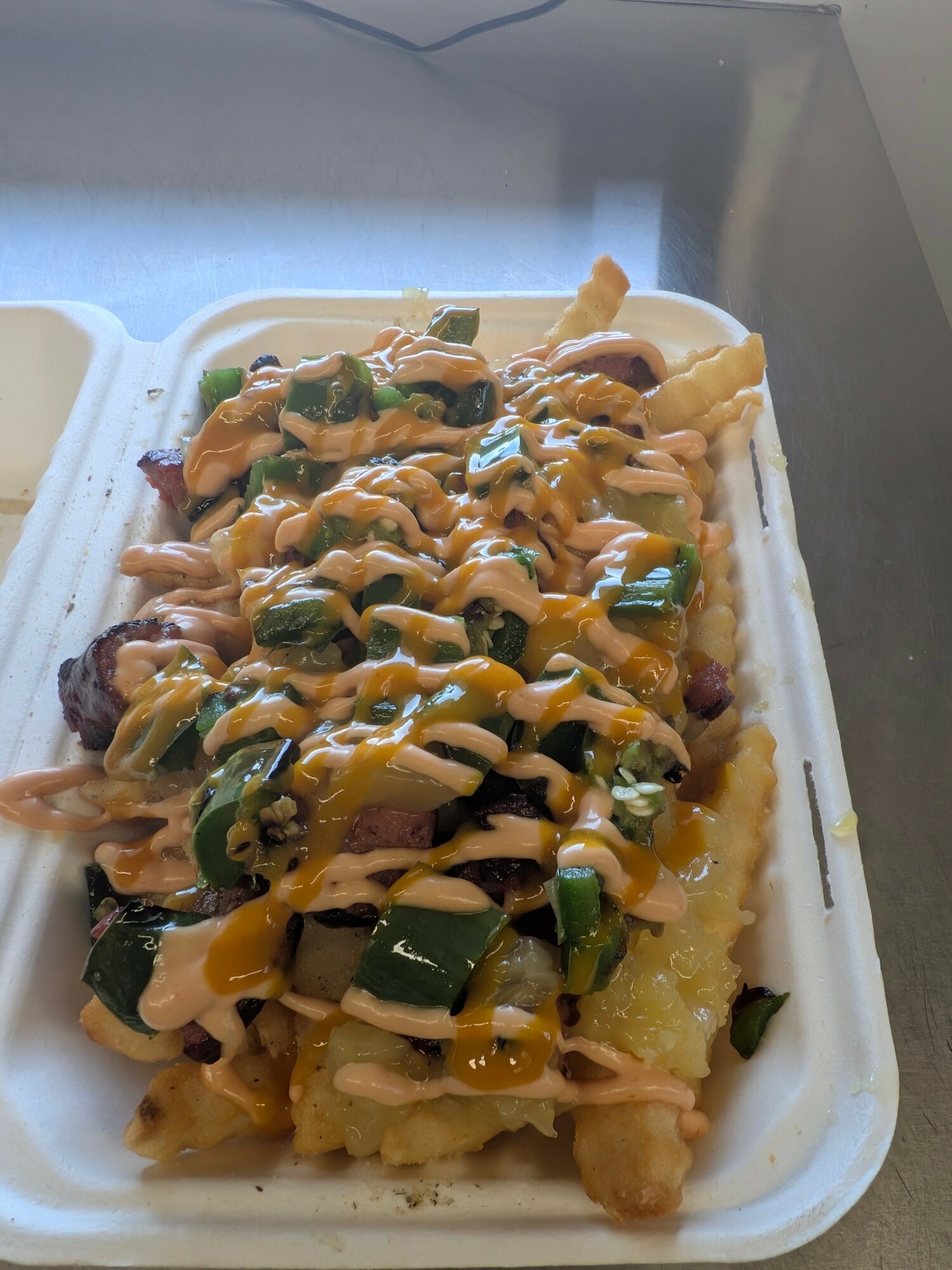 Fried food topped with chopped green onions, drizzled with yellow sauce, served on a white foam tray.