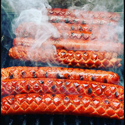 Barbecue sausages with grill marks and smoke, arranged on a grill.