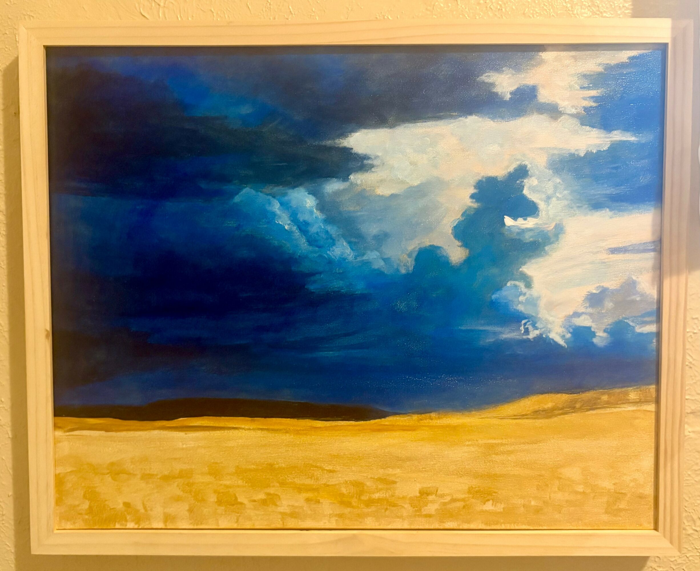 Landscape painting with a dark blue stormy sky and a golden field below, framed in wood.