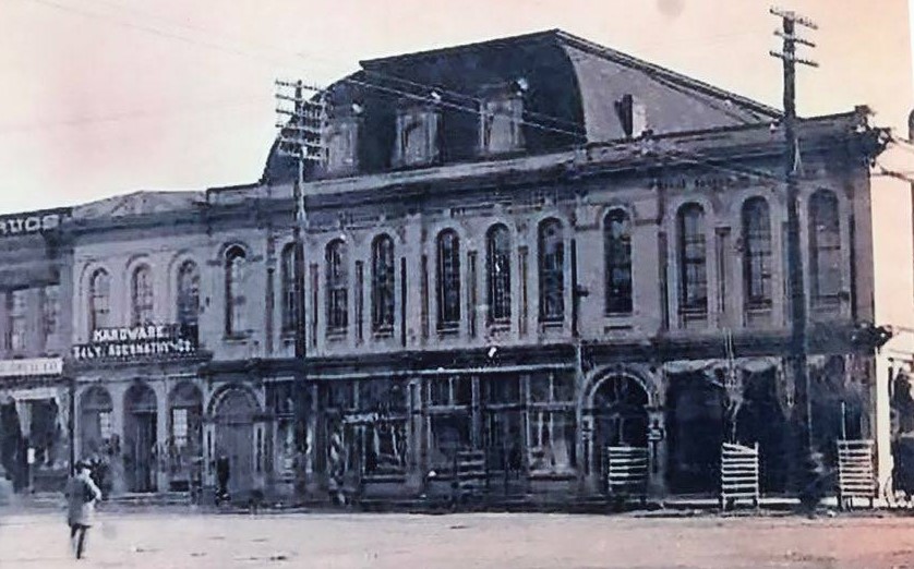 Old building with multiple stories, arched windows, and a storefront on the ground level, with utility poles nearby.