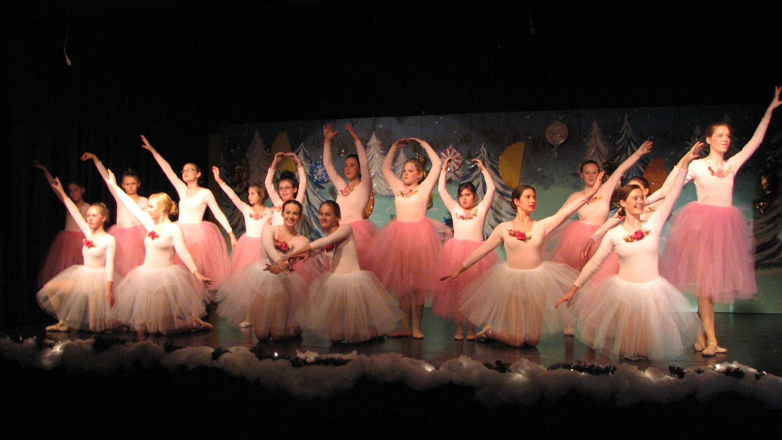 Group of ballet dancers in pink tutus performing on stage with arms raised and arms extended.