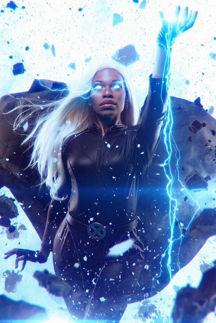 Woman with long blonde hair and glowing eyes raises her hand, summoning lightning amidst a splash of blue and black debris.