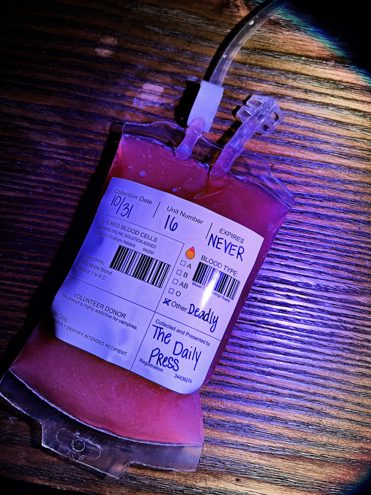 Blood bag with tubes on wooden surface, label visible, blood appears dark red, lighting is dim.