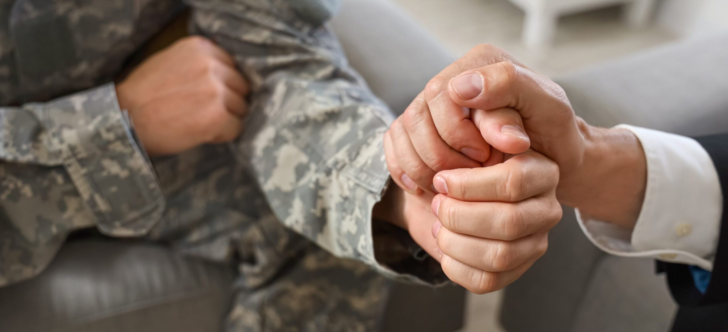 A person in military uniform holding hands with another person in a suit, showing support and connection.