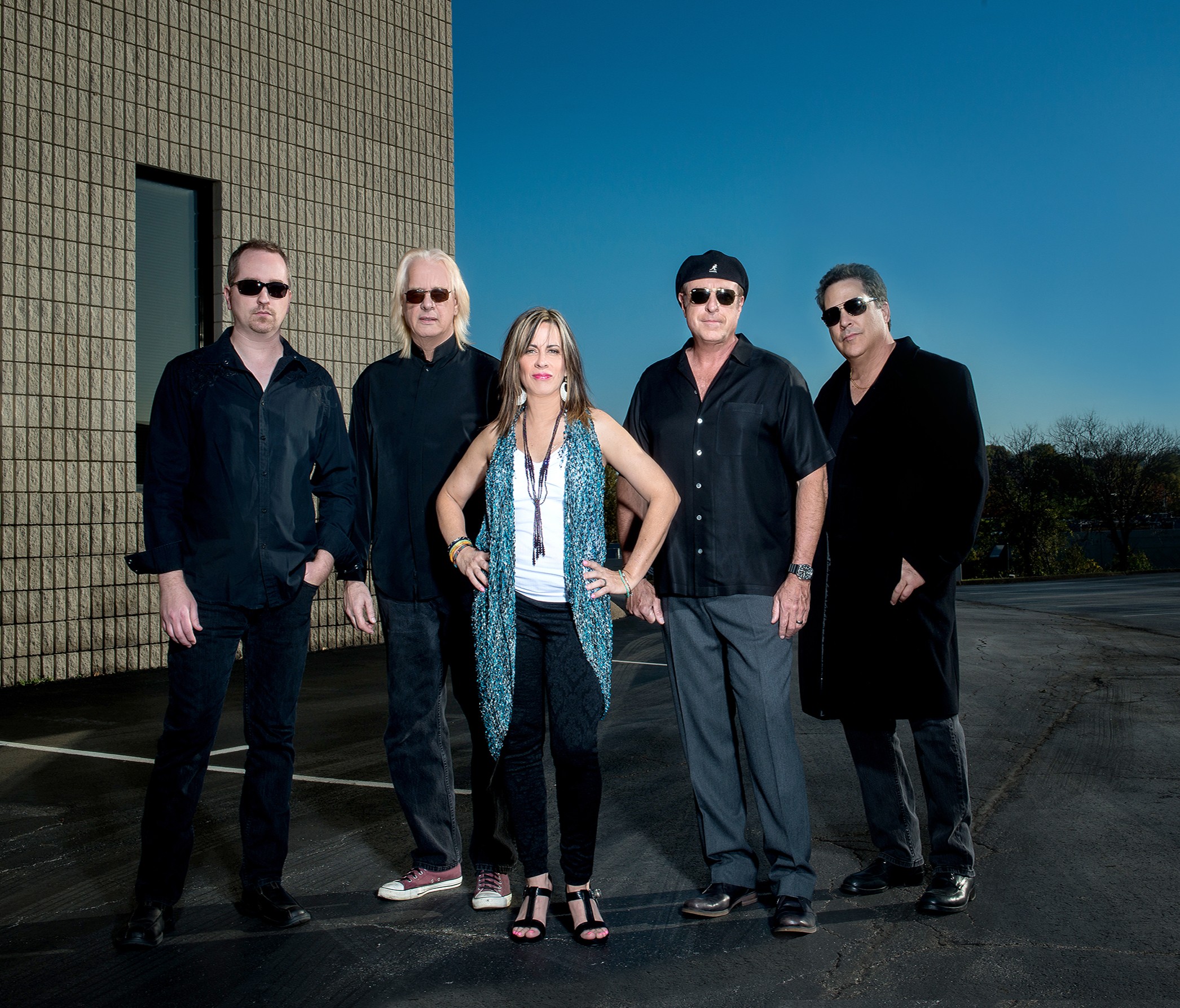 Group of five people standing outdoors against a building and sky, posing for a photo.