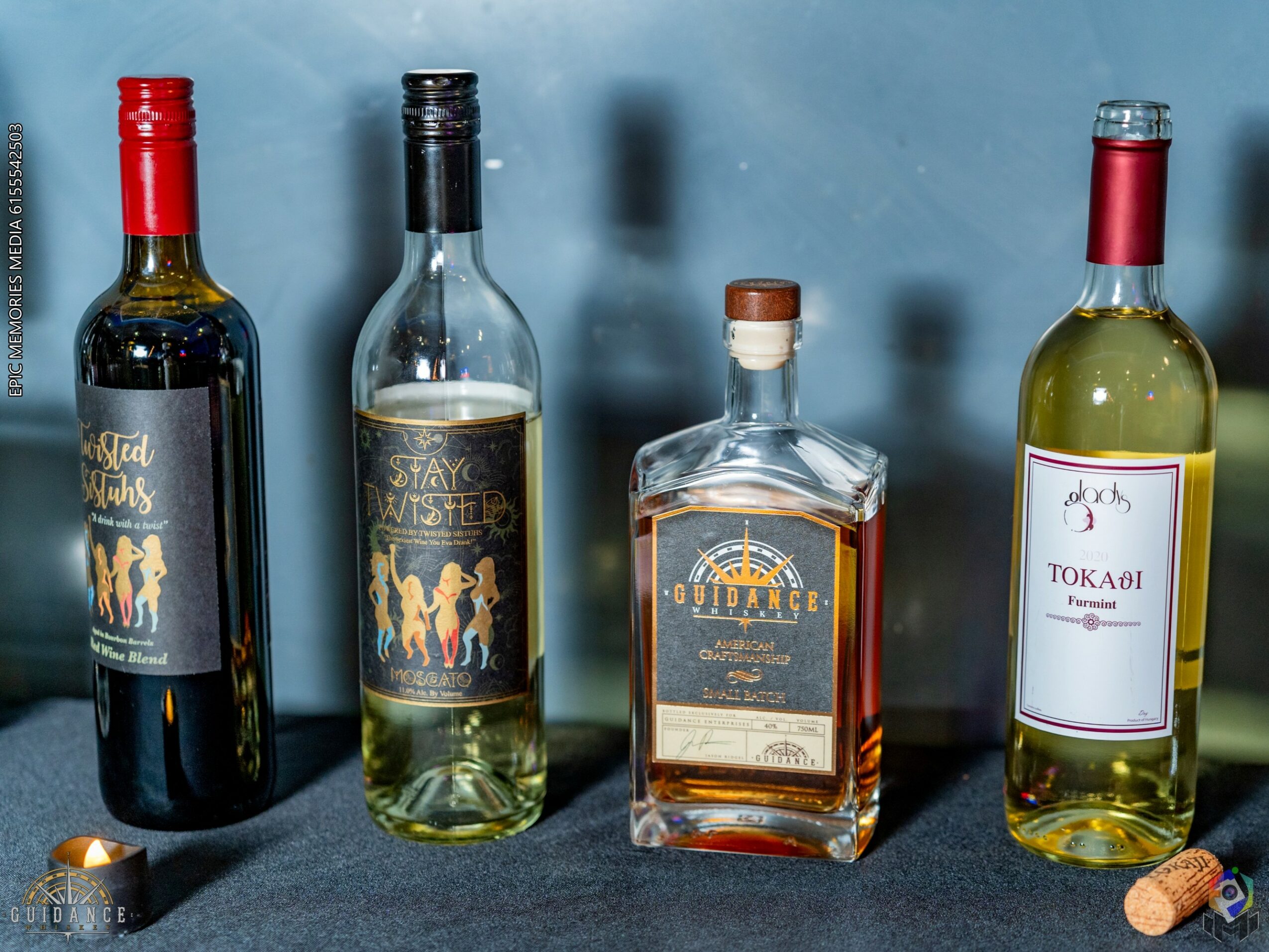 Four bottles of alcohol on a blue surface, with a cork and cap nearby, against a blue background.