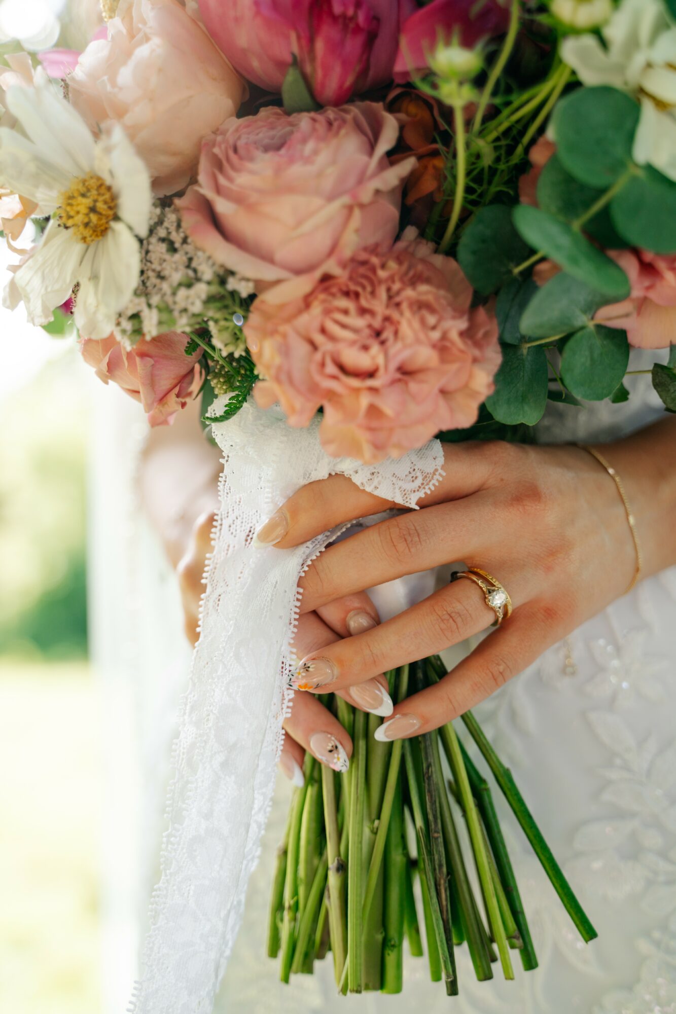 Person holding a bouquet of pink and white flowers with green leaves, wearing rings and a lace garment.
