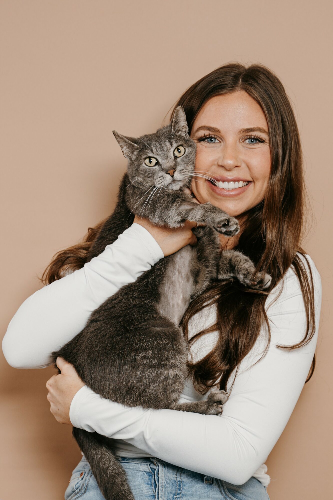 Woman smiling and holding a gray tabby cat against a beige background.
