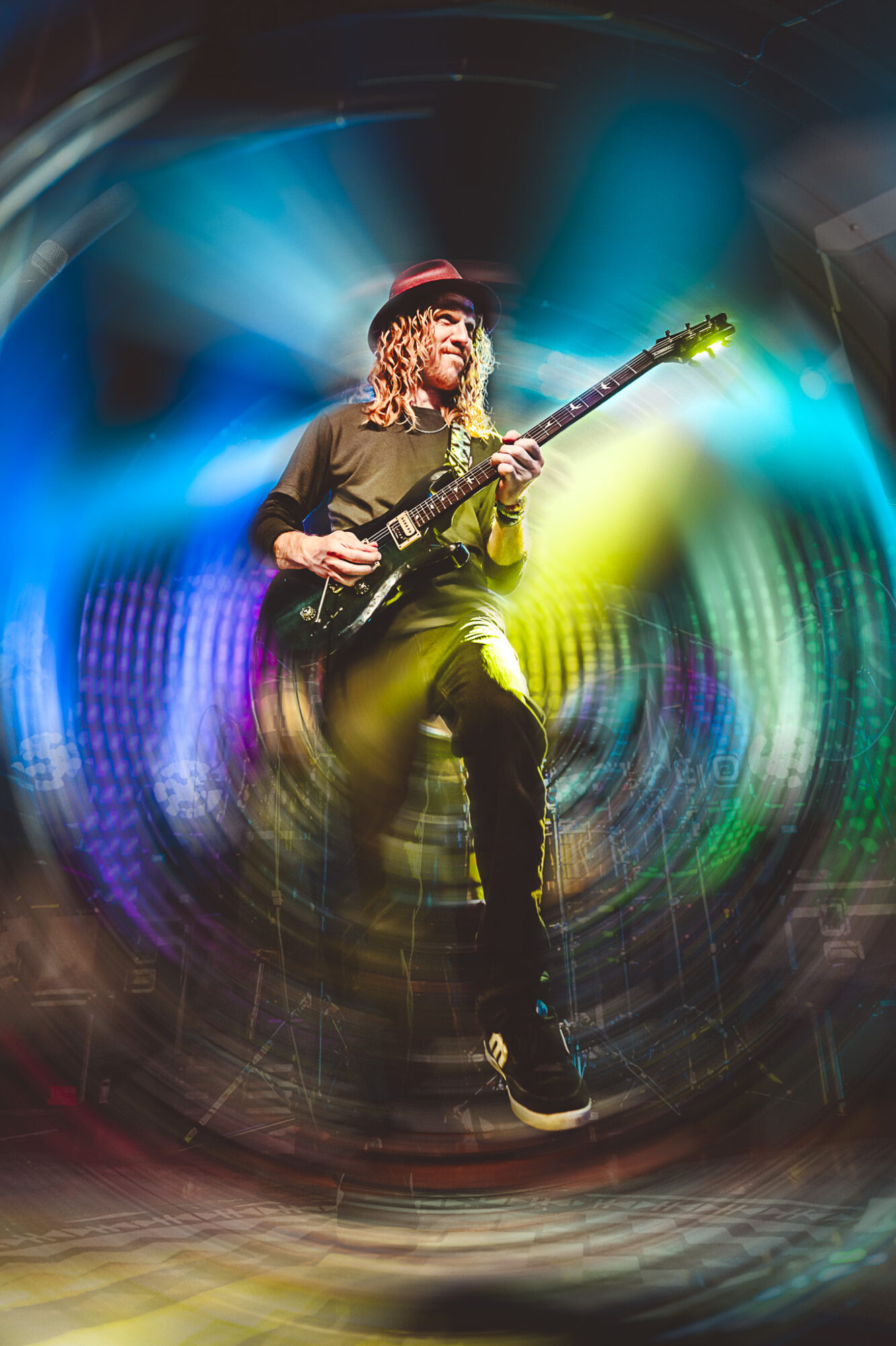 Musician playing guitar on stage with colorful lights and motion blur effects.