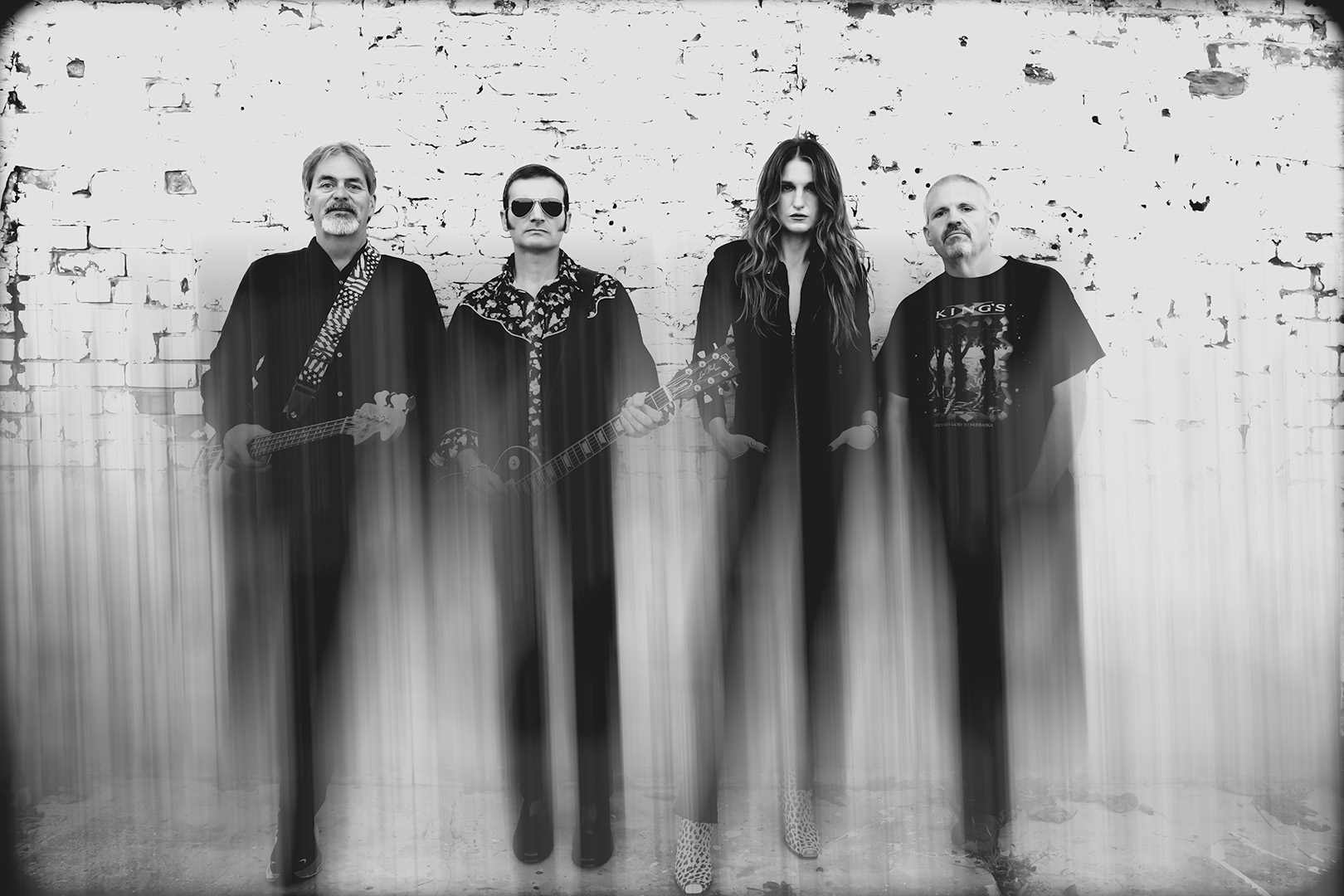 Four people standing against a brick wall, with a distorted, vertical streak effect, in black and white.