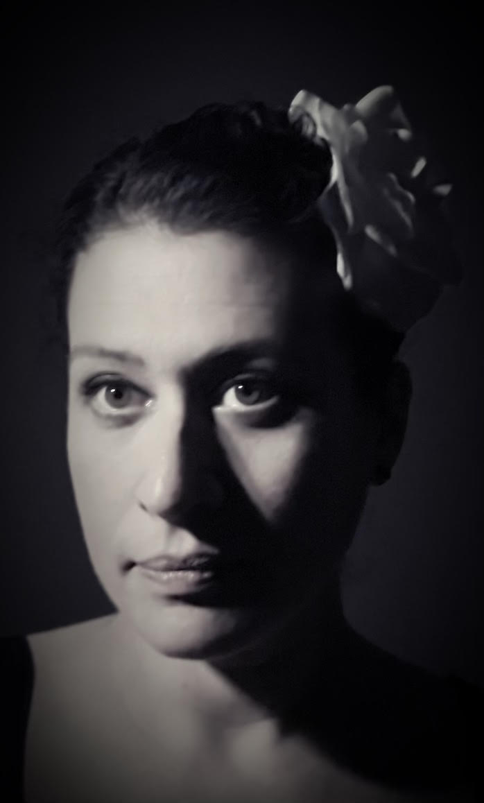 Black and white portrait of a woman with a large bow in her hair, looking directly at the camera.