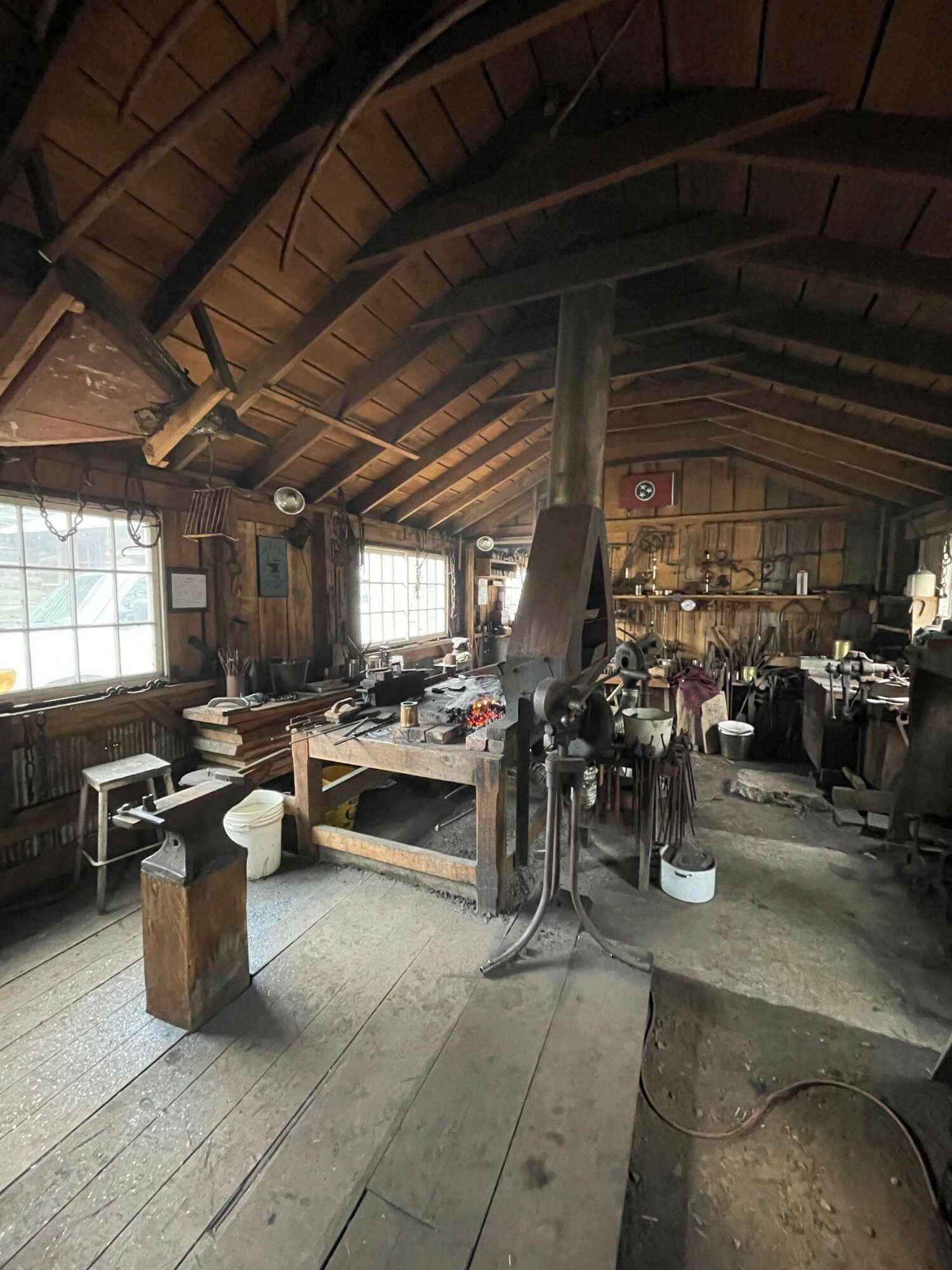 Workshop with wooden ceiling, large window, workbenches, tools, and equipment, viewed from a tilted angle.