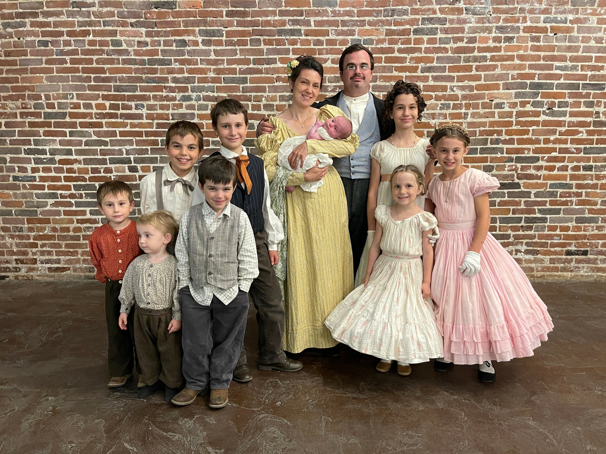 Family of ten posing in front of a brick wall, including adults and children in formal attire.